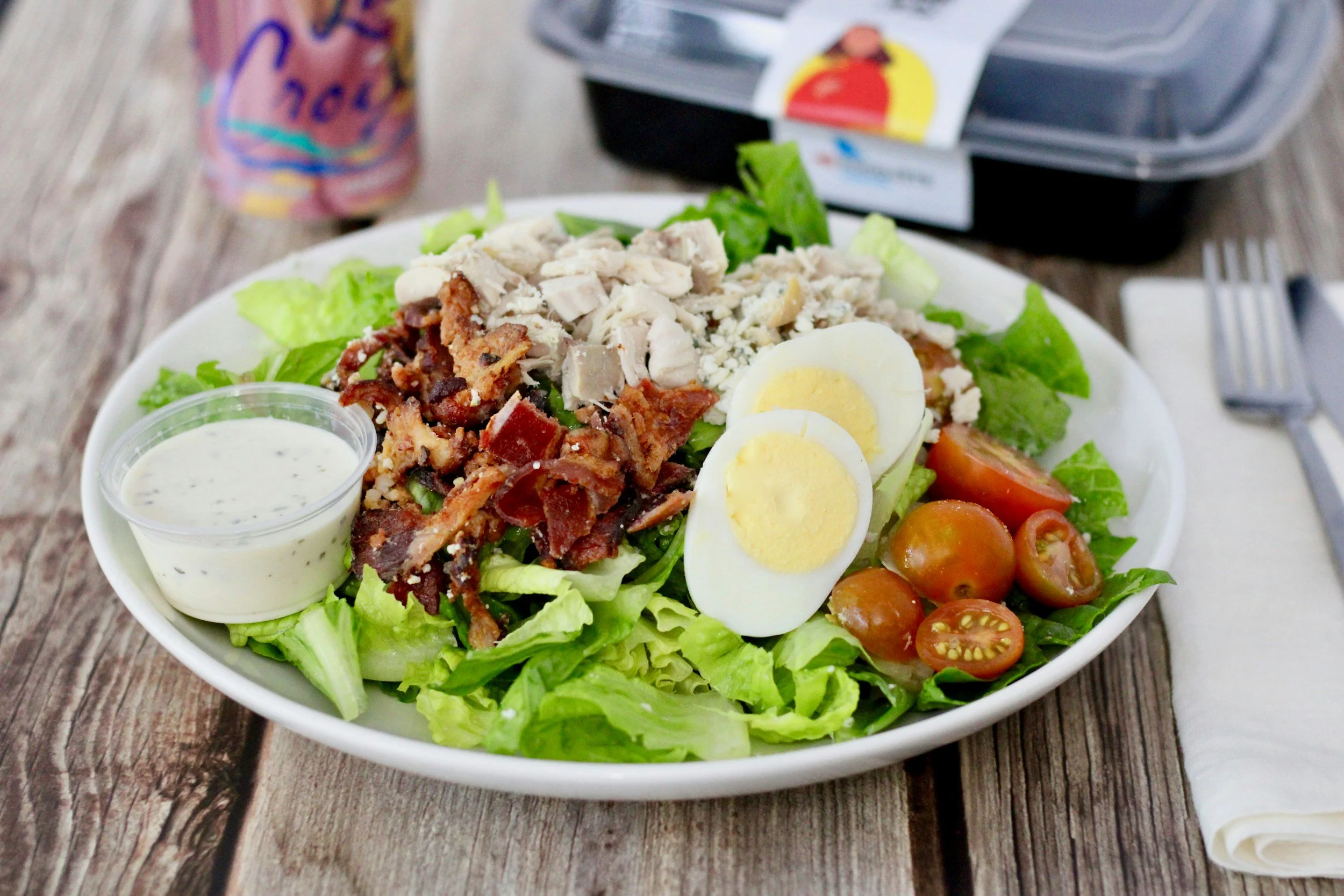 A salad with boiled eggs, lettuce, bacon, tomatoes, and ranch on a table