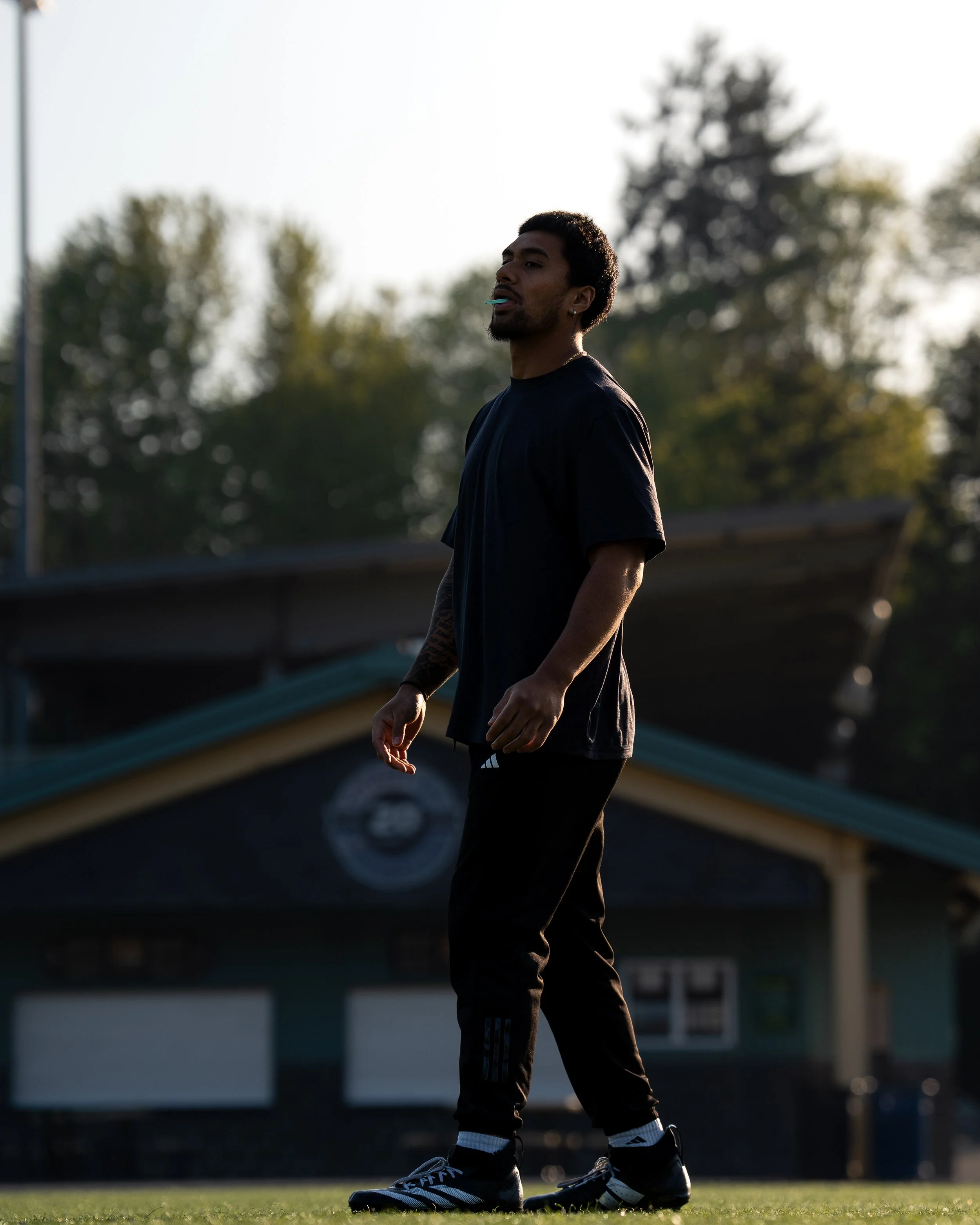 Coach Alphonzo walking across an athletic field with a sun setting in the background