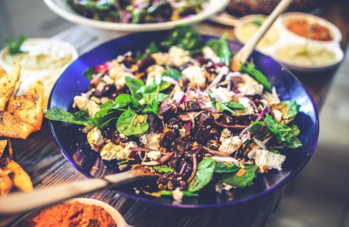 A colorful salad inside a blue bowl on a table full of colorful, healthy foods