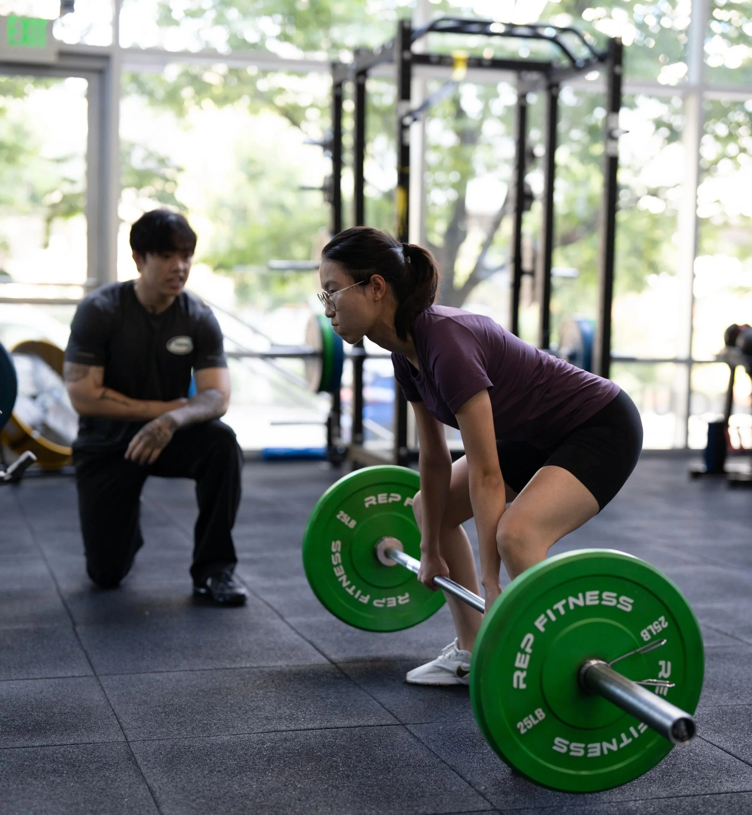 A bStrong member performs a deadlift exercise with her coach providing feedback