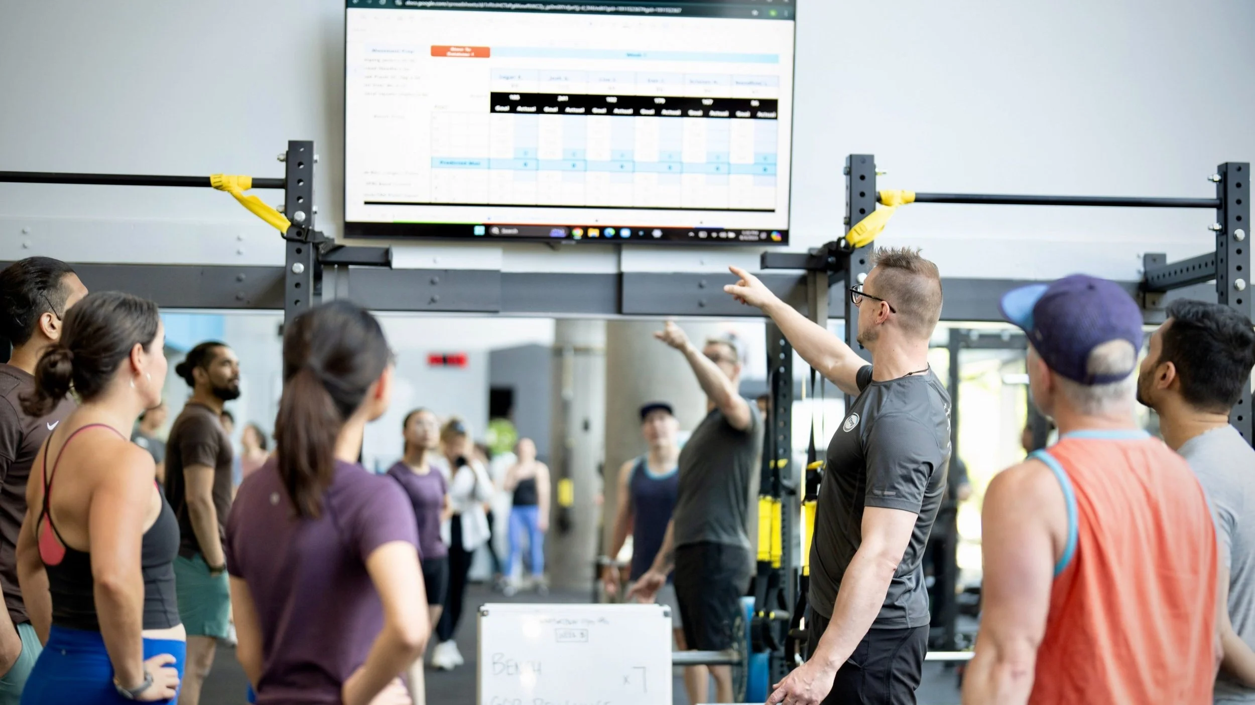 Coach Blake pointing to the screen with a small group of members watching to see what the workout looks like for the day.