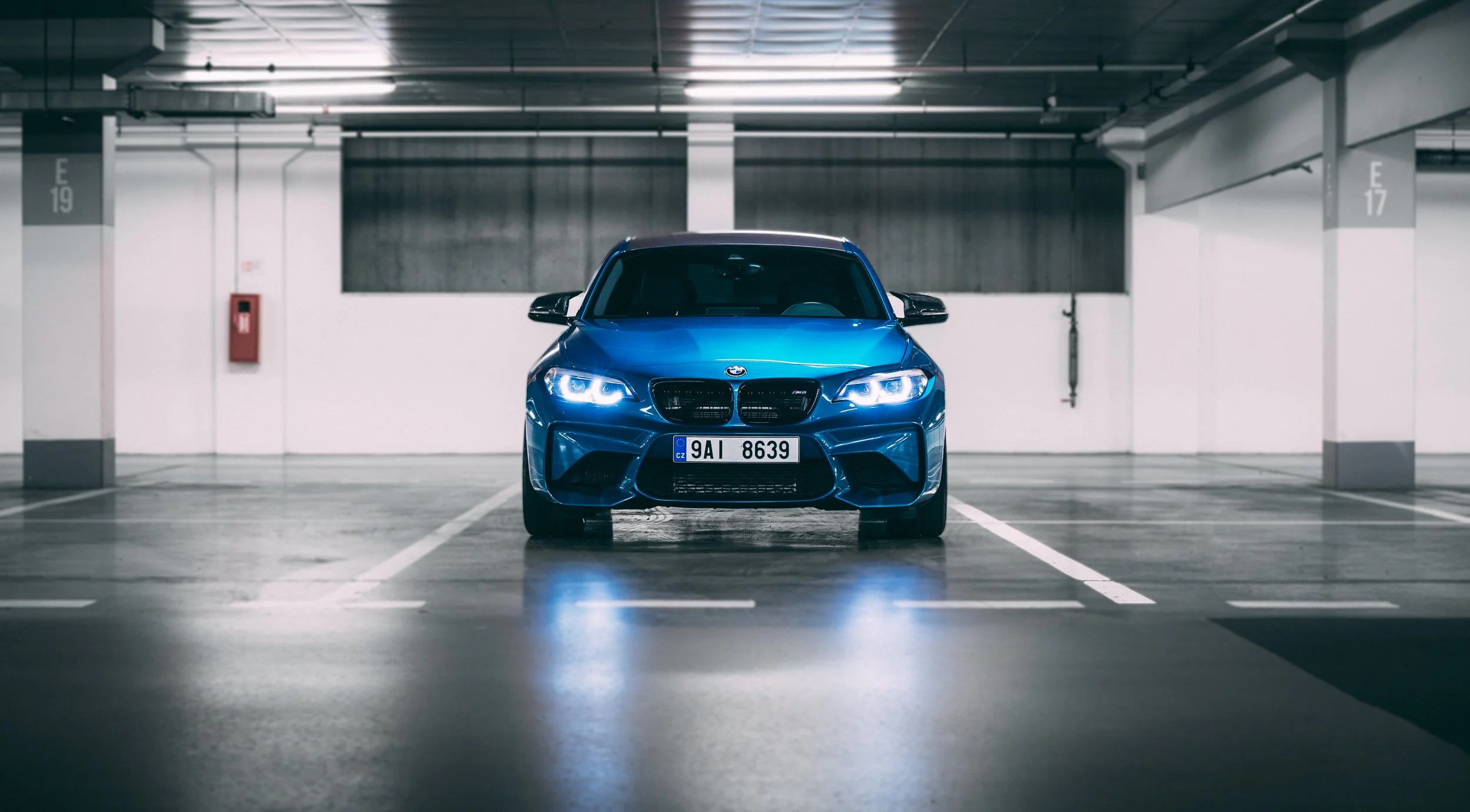 Blue car with illuminated headlights in empty parking garage