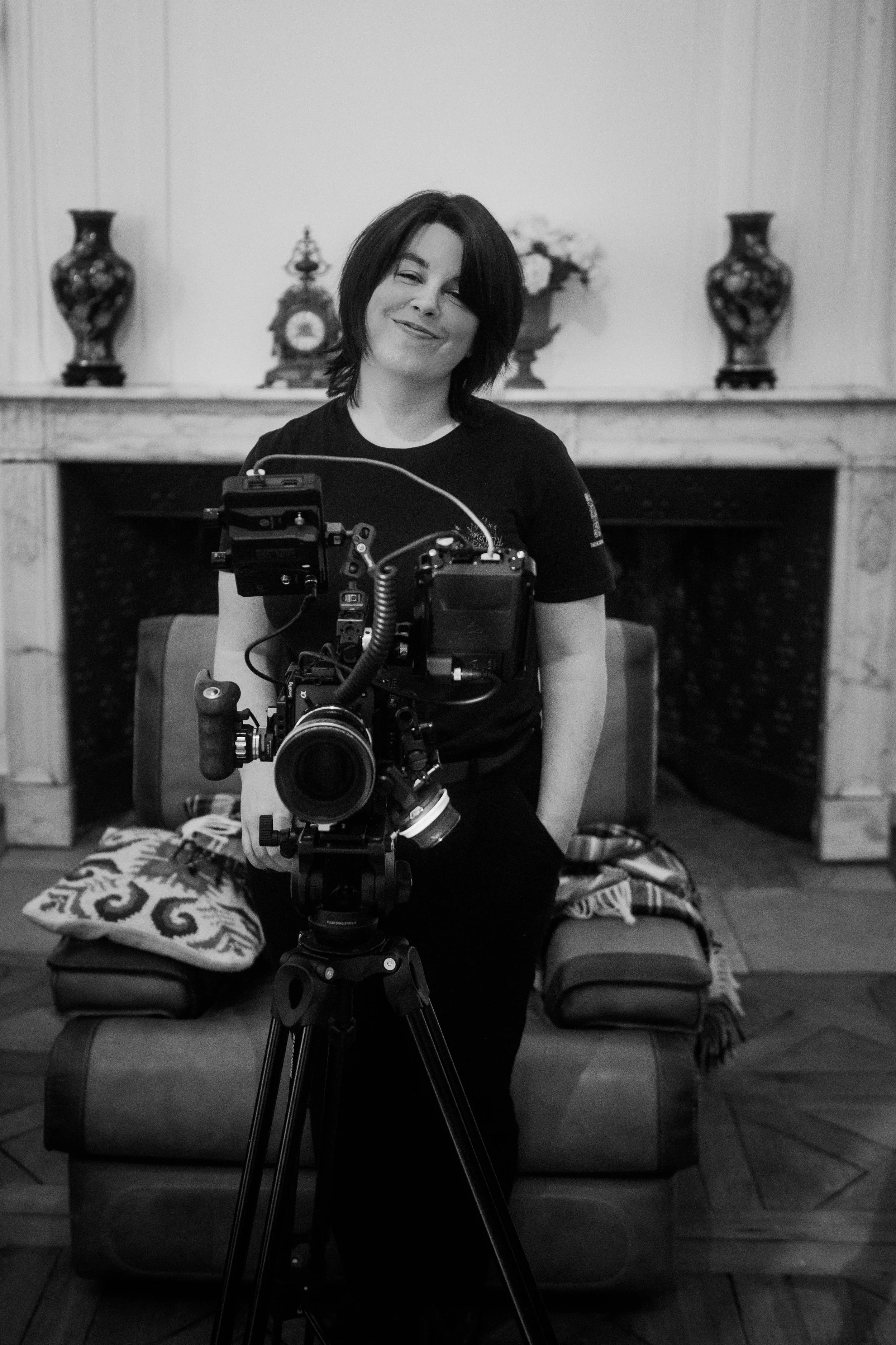 Une femme souriante derrière une caméra professionnelle en intérieur.