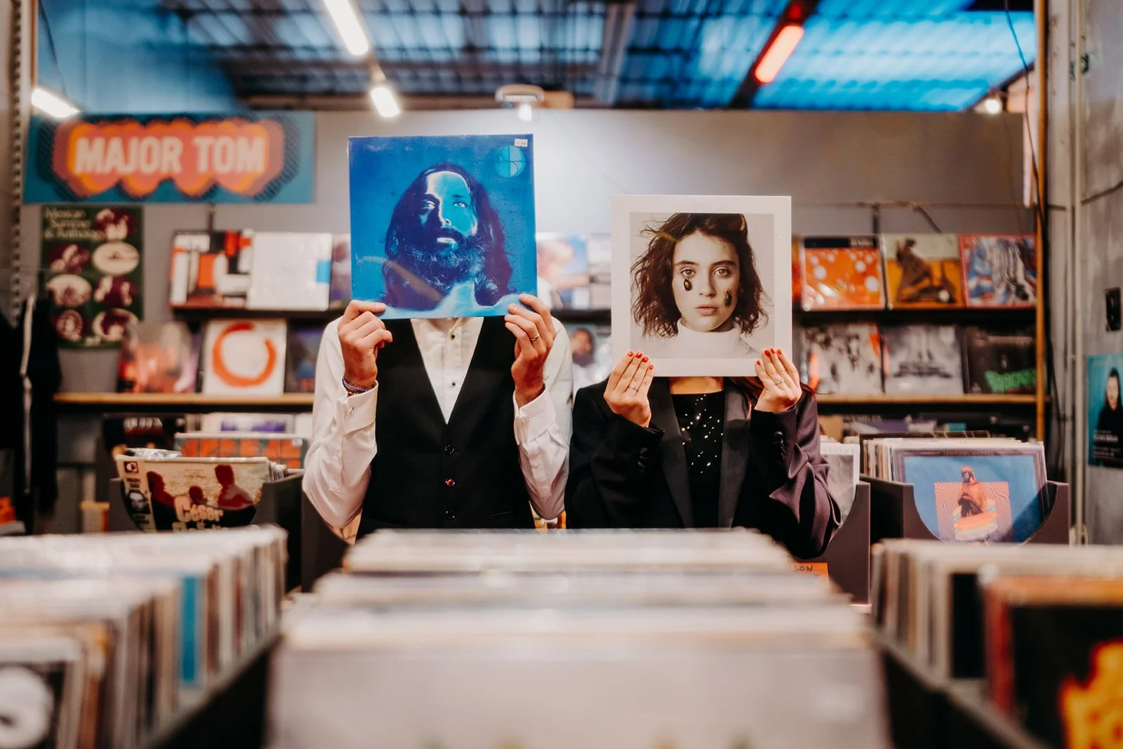 Deux personnes portant des photos pour visages devant leur visage, dans une librairie de disques.