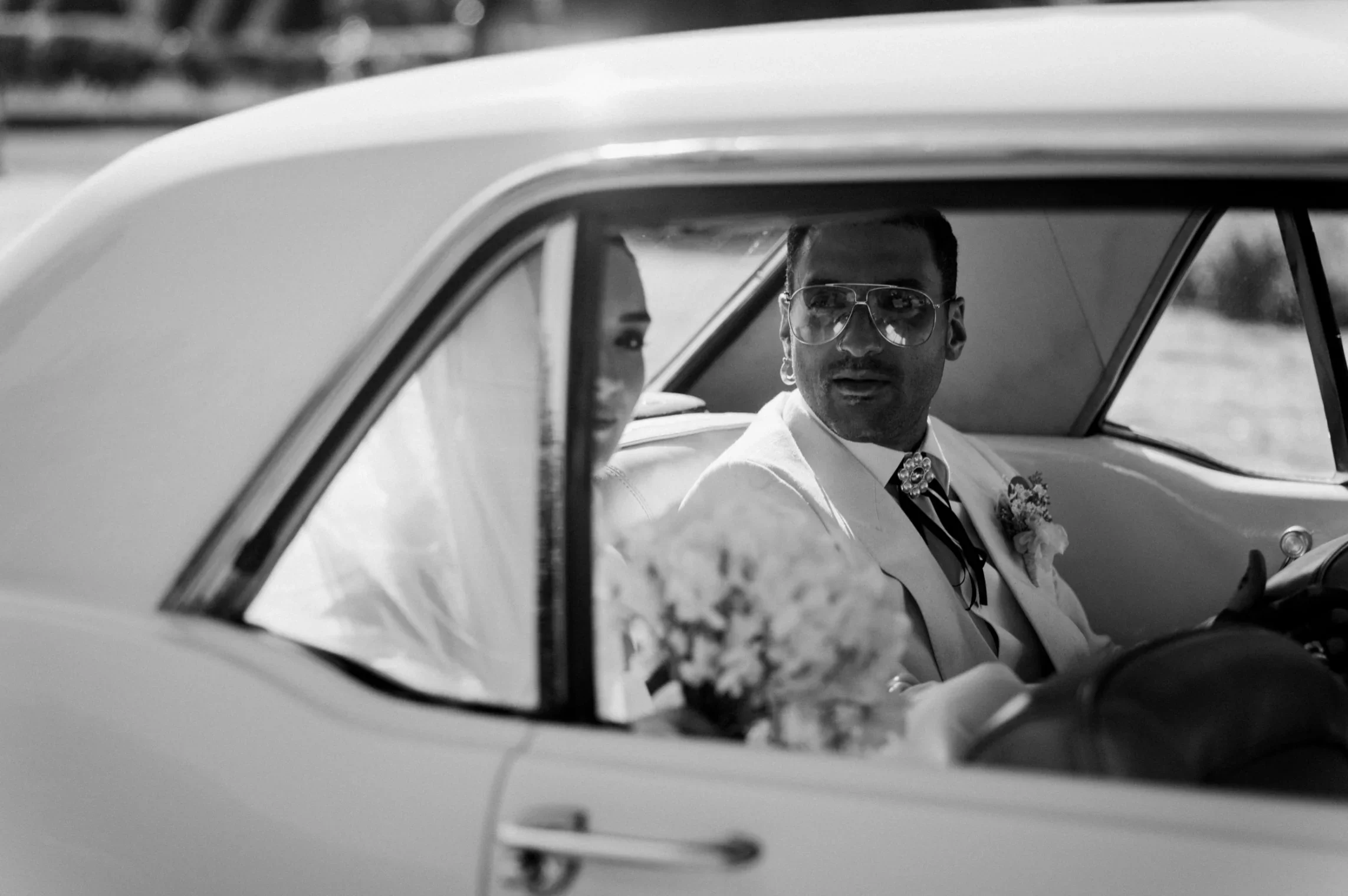 portrait-groom-costume-voiture-vintage-lunettes-cinematique-noir-blanc-photographe-mariage-video-mariage-the-wild-strawberry.webp