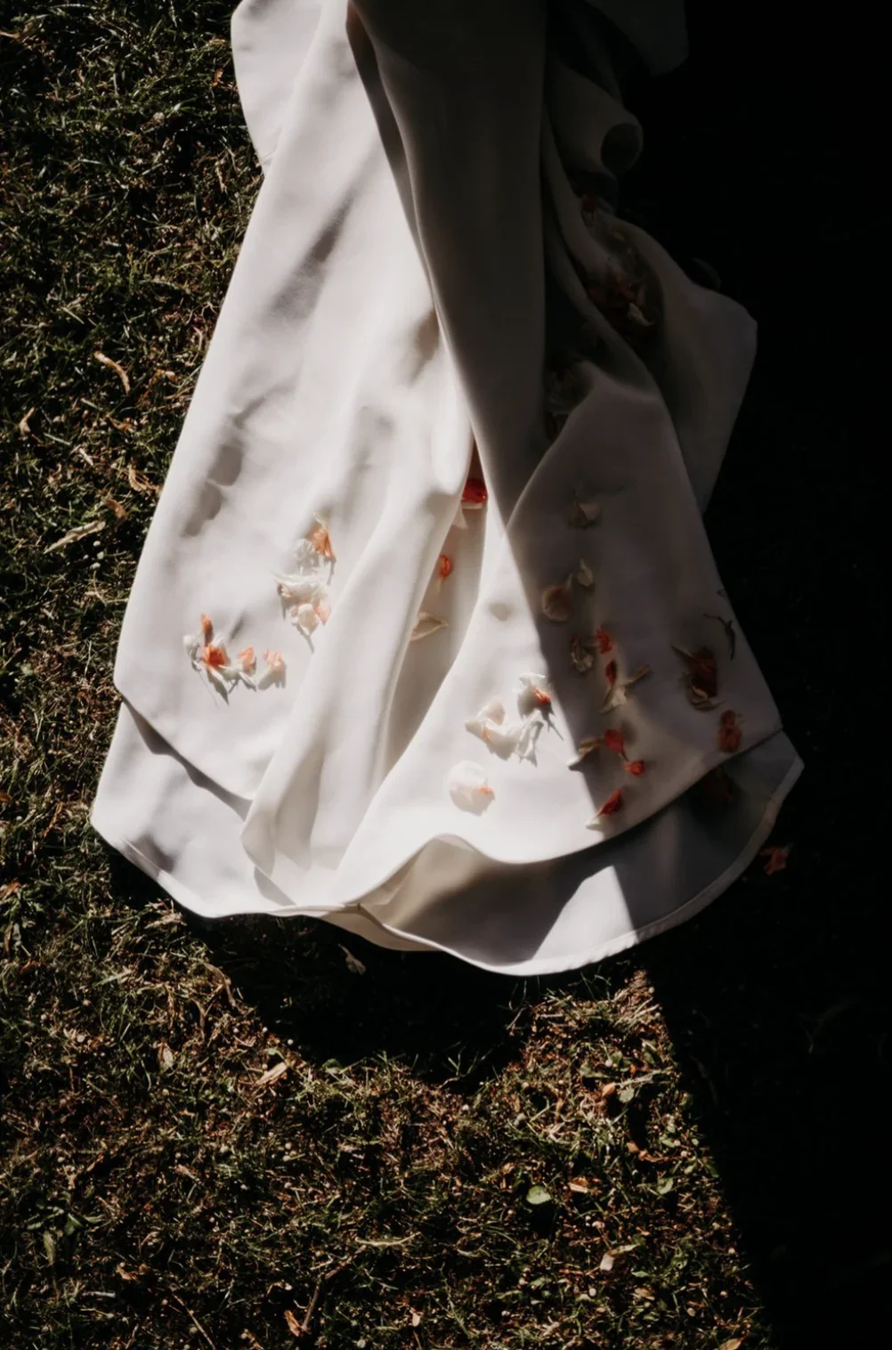 robe-de-mariee-traine-petales-roses-pelouse-editorial-photographe-mariage-video-mariage-the-wild-strawberry.webp