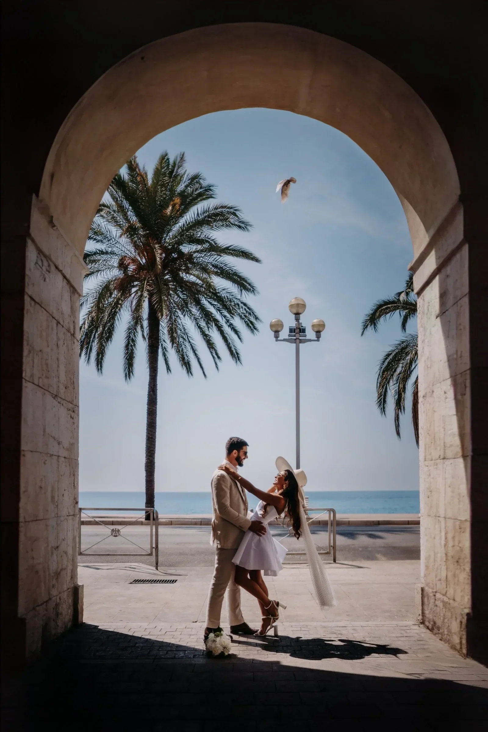 mariage-nice-cote-azur-couple-sous-arche-palmiers-bord-mer-photographe-mariage-video-mariage-the-wild-strawber.webp