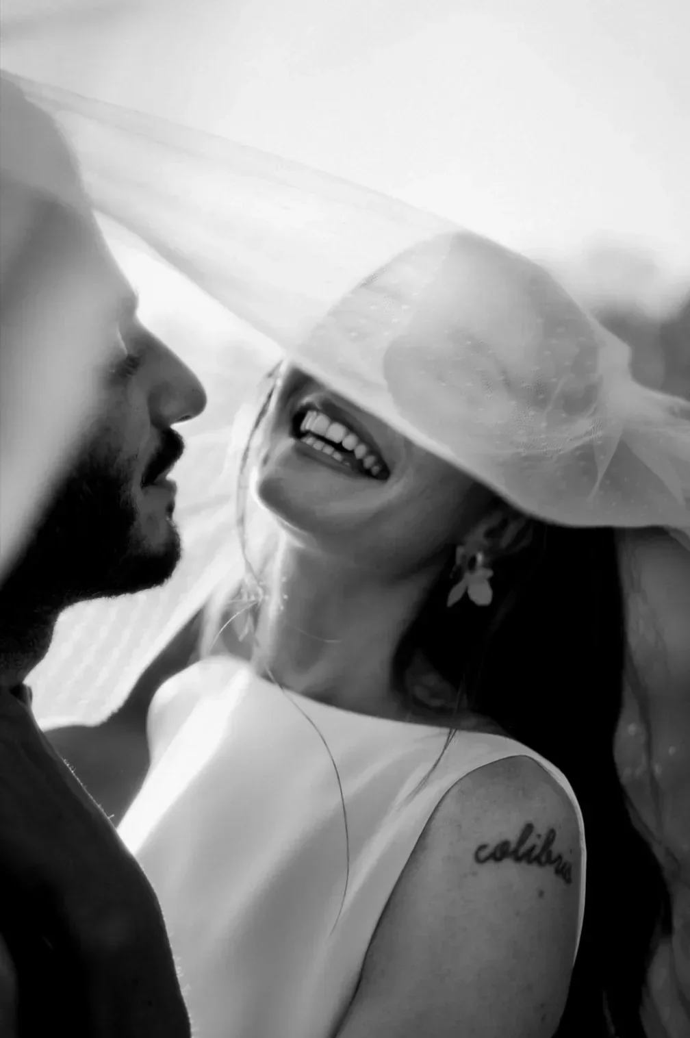 portrait-mariee-rires-sous-voile-groom-noir-blanc-photographe-mariage-film-mariage-the-wild-strawberry.webp