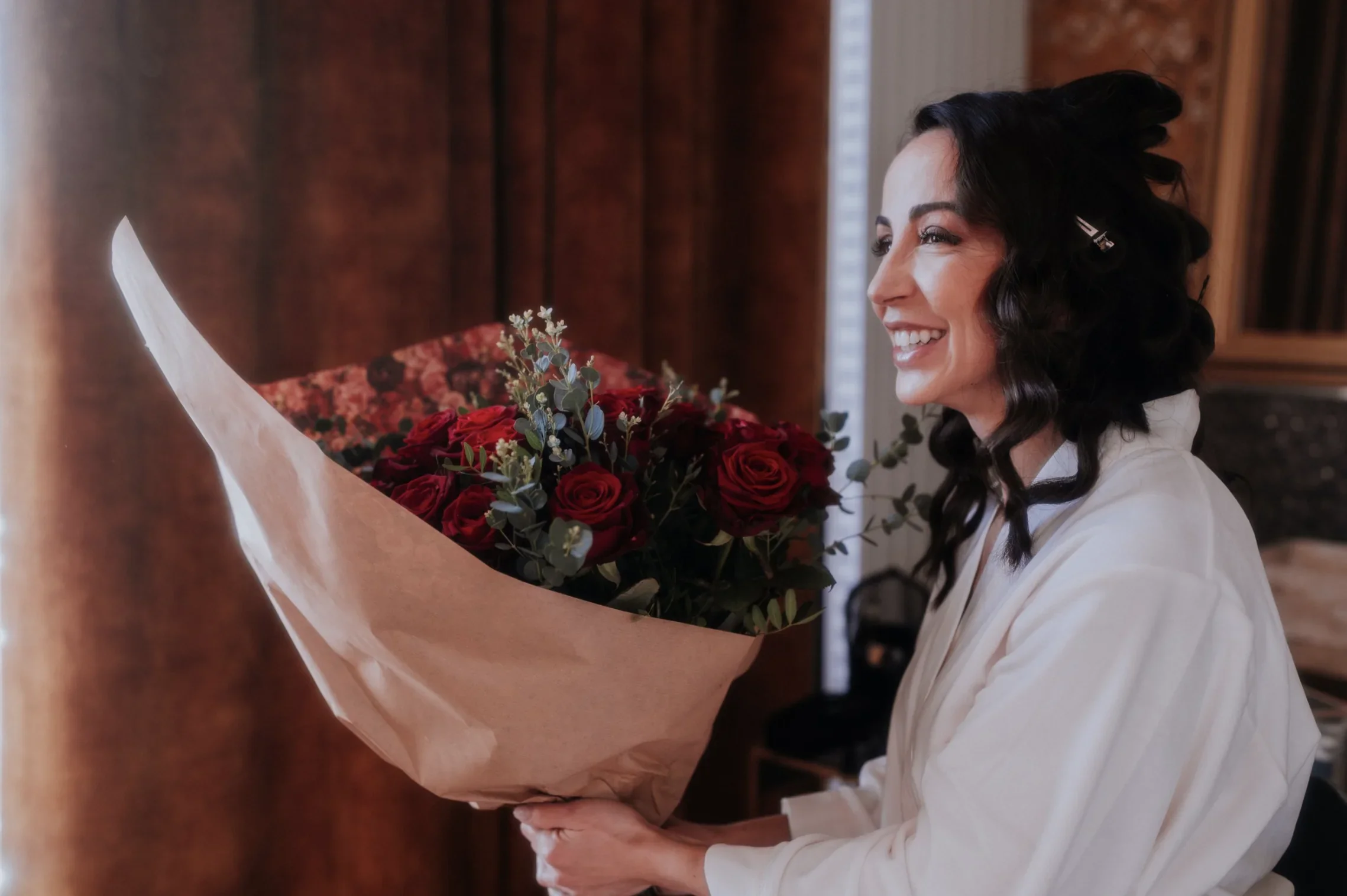 preparatifs-mariee-peignoir-bouquet-roses-rouges-joie-getting-ready-photographe-mariage-video-mariage-the-wild-strawberry.webp