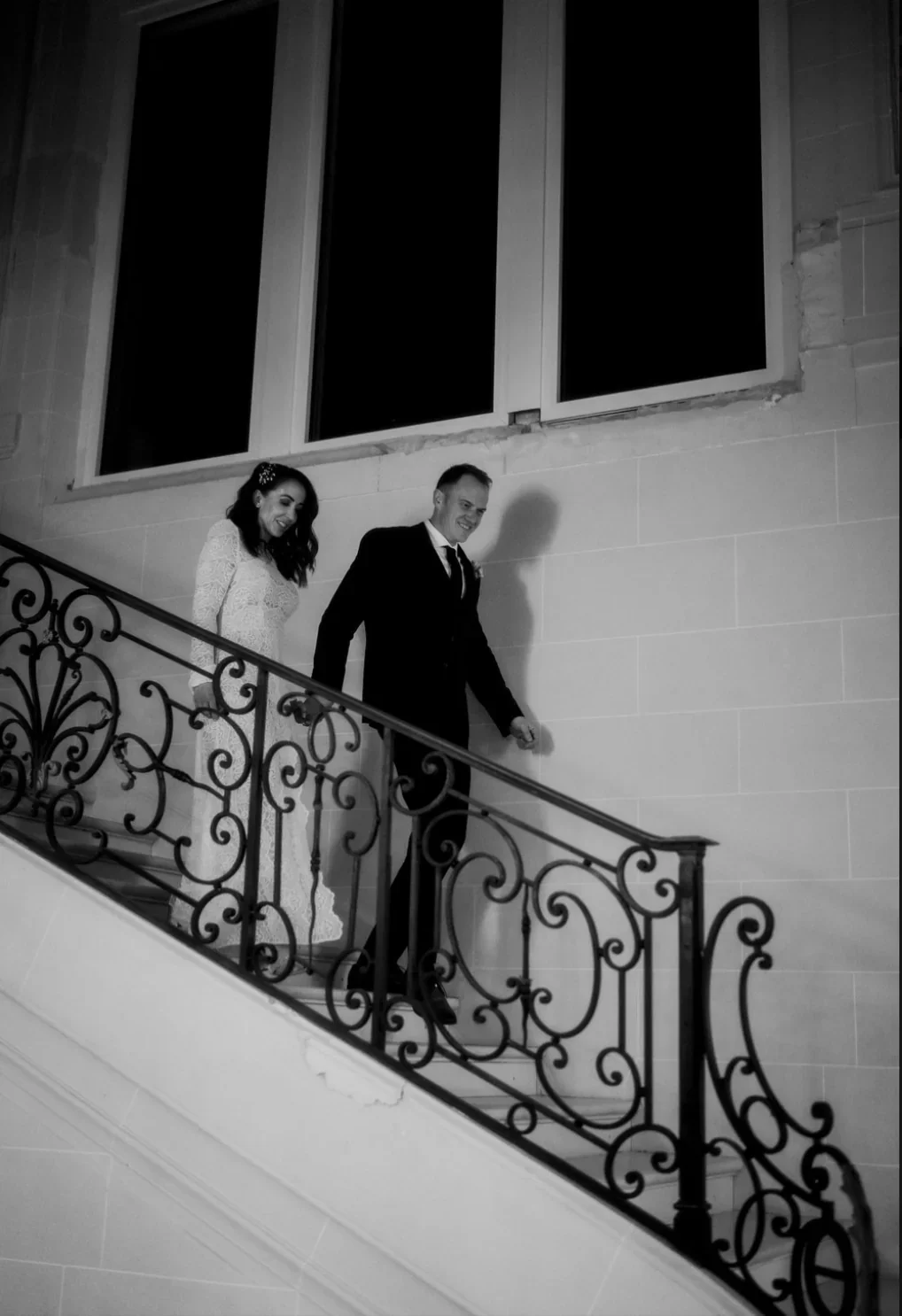 portrait-couple-maries-escalier-fer-forge-chateau-nuit-noir-blanc-photographe-mariage-film-mariage-the-wild-strawberry.webp