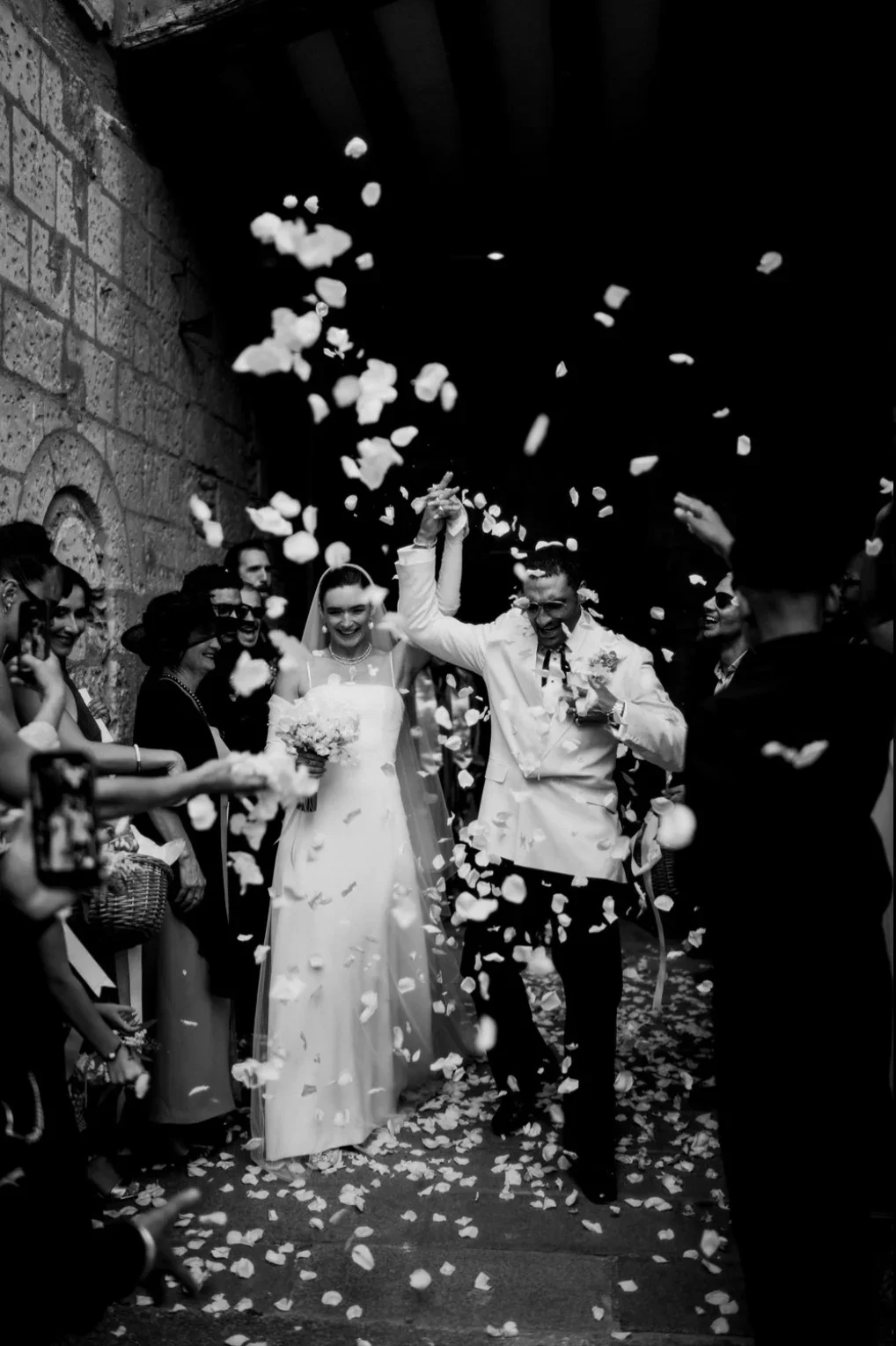 sortie-ceremonie-maries-petales-blancs-tunnel-noir-blanc-cinematique-photographe-mariage-video-mariage-the-wild-strawberry.webp
