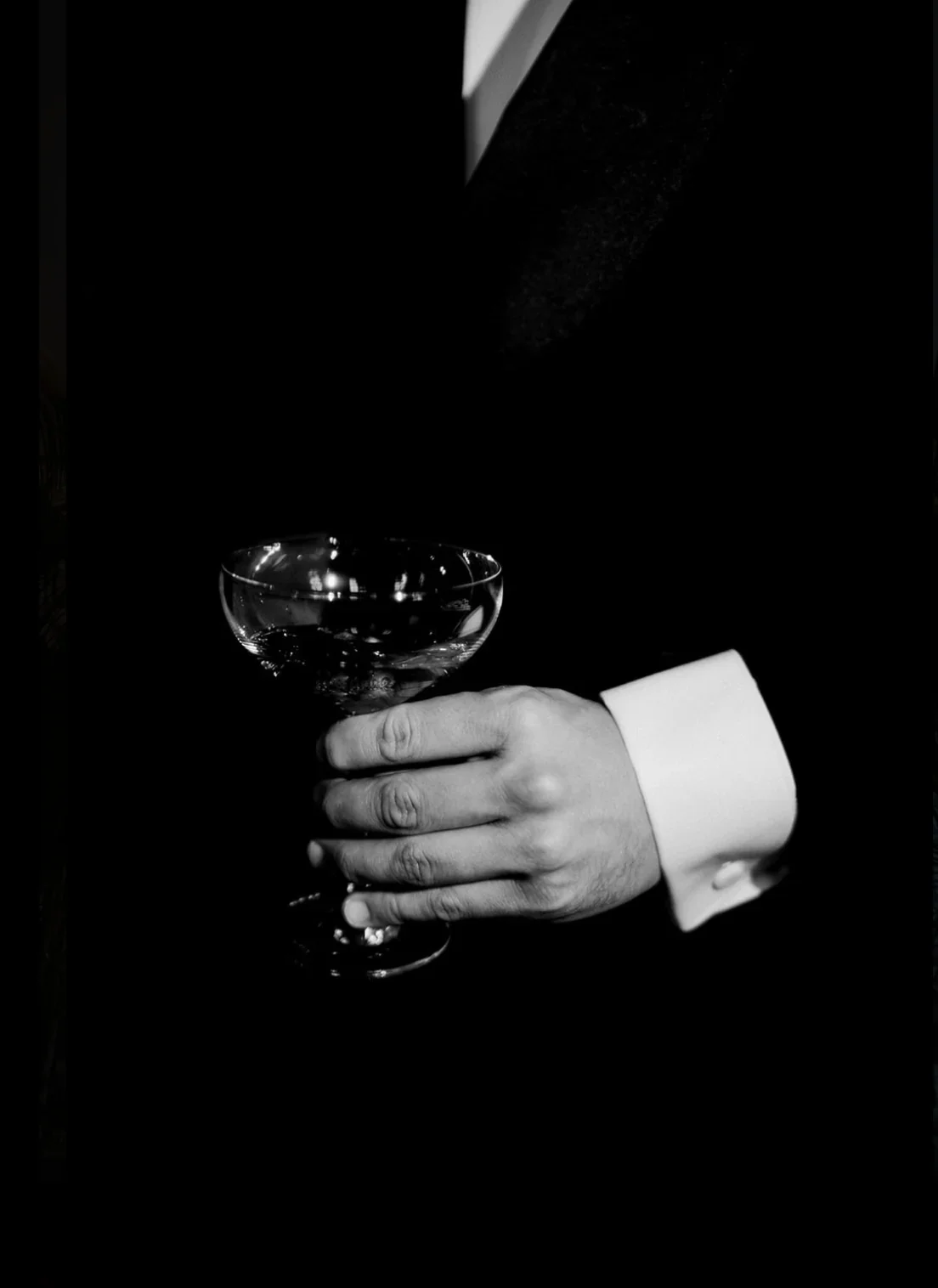 vin-dhonneur-main-coupe-champagne-groom-costume-elegant-noir-blanc-photographe-mariage-video-mariage-the-wild-strawberry.webp