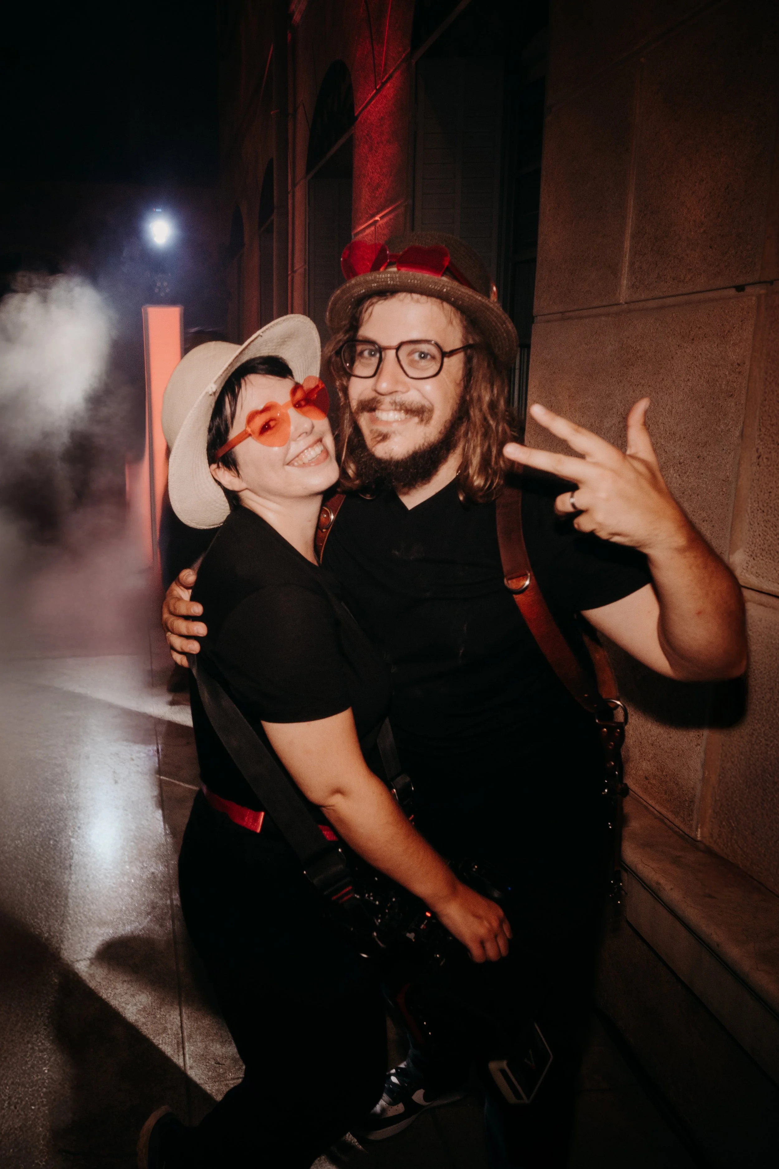 Deux personnes souriantes déguisées avec des chapeaux et des lunettes, posant ensemble lors d'une fête ou évènement