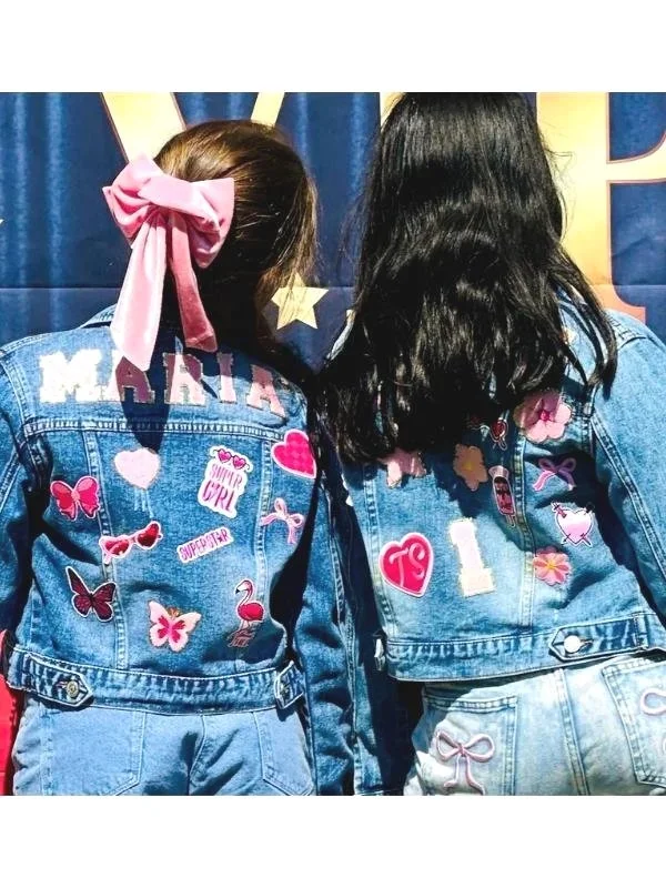 Two children showing the backs of their personalised denim jackets, decorated with names, butterflies and heart patches.
