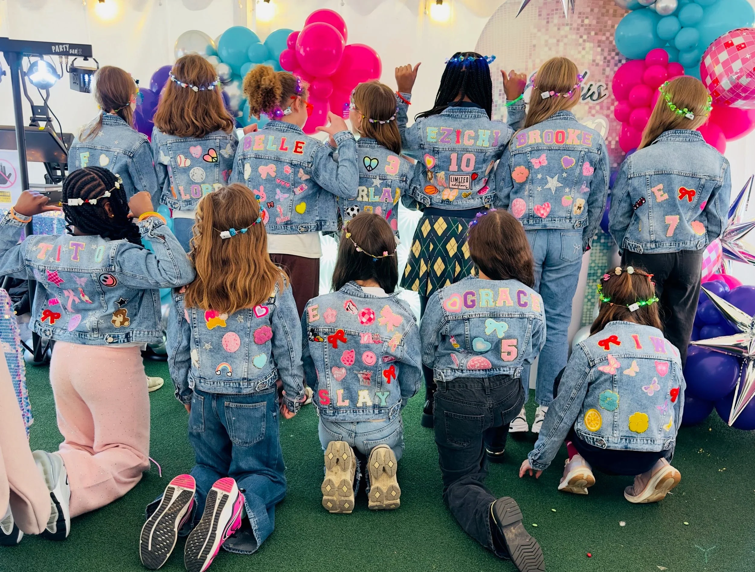 Children pictured from behind wearing denim jackets personalised with colourful names, butterflies and heart patches at a Luvlybubbly party.