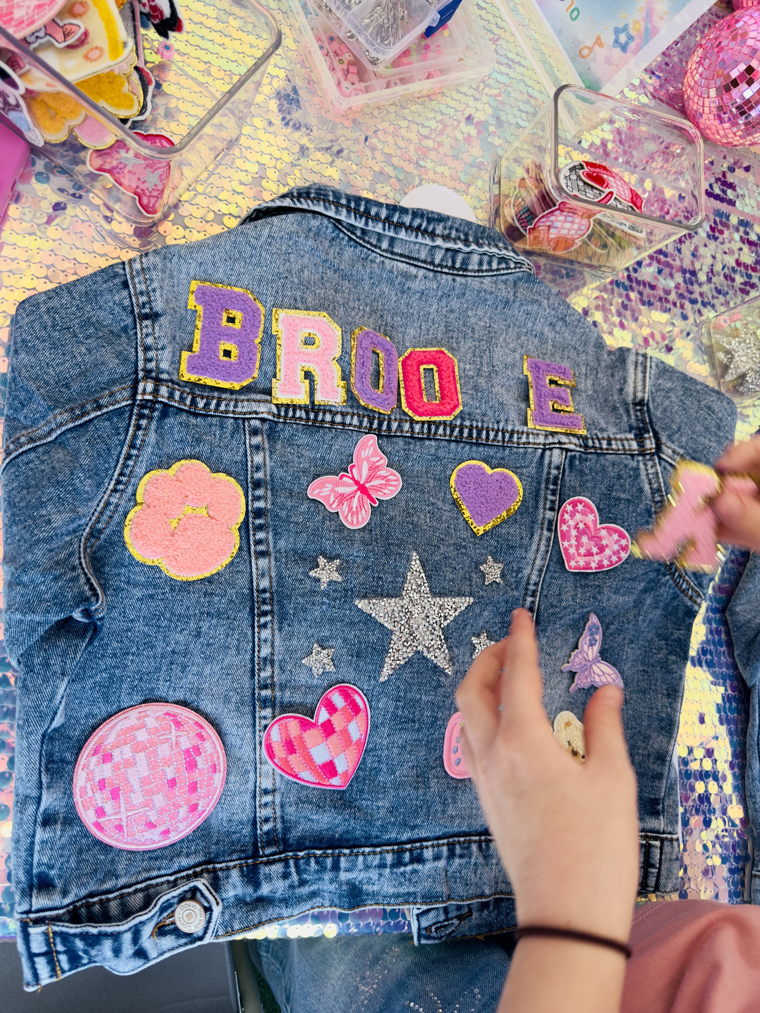 Child arranging pastel letter patches on a denim jacket during a Luvlybubbly jacket customising party.