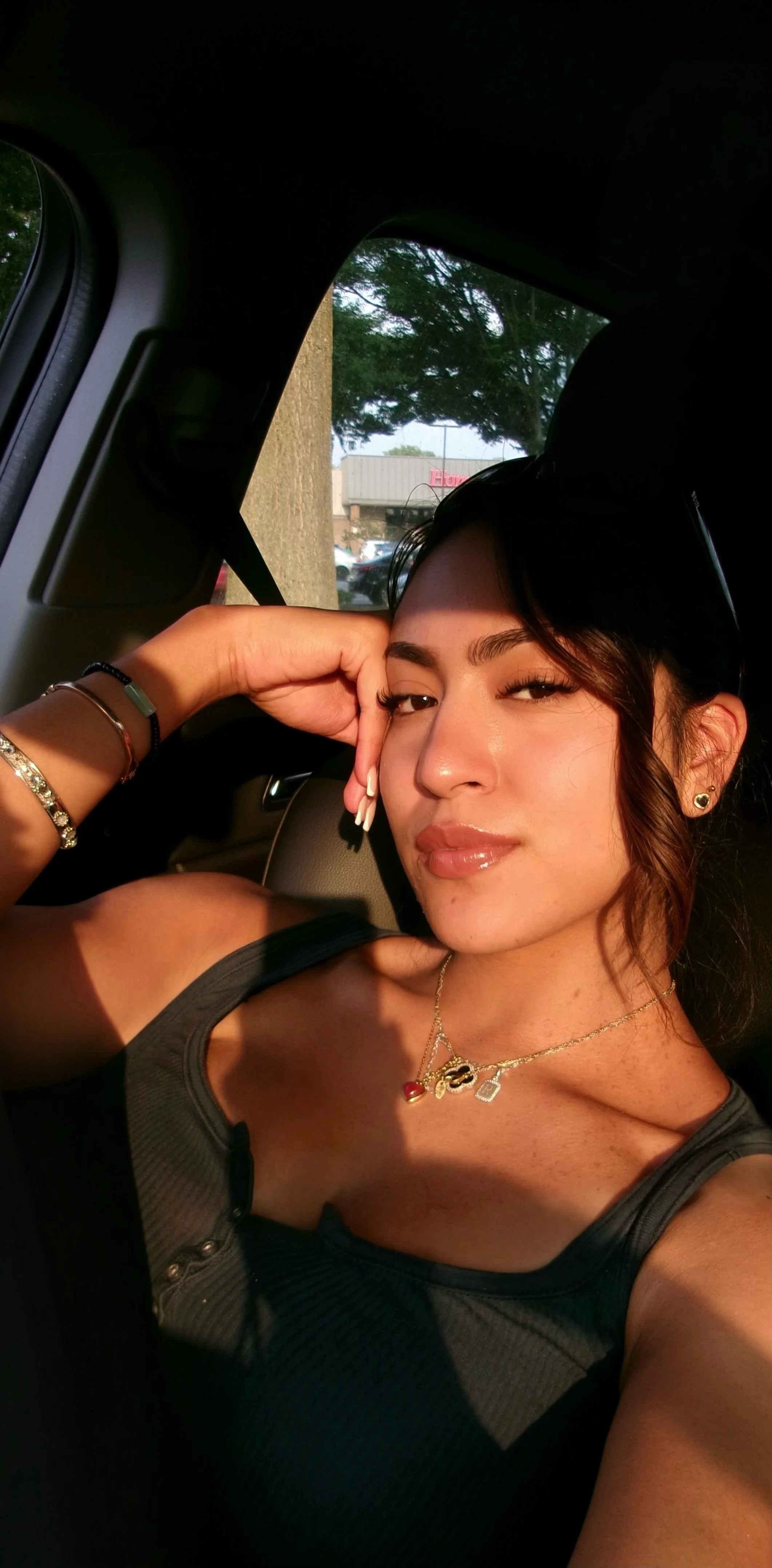 A young woman with dark hair, smiling in the sunlight, in a car