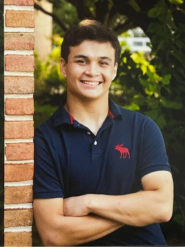OCC Consultant Christopher Hyre, smiling and standing against a brick wall in a blue shirt.