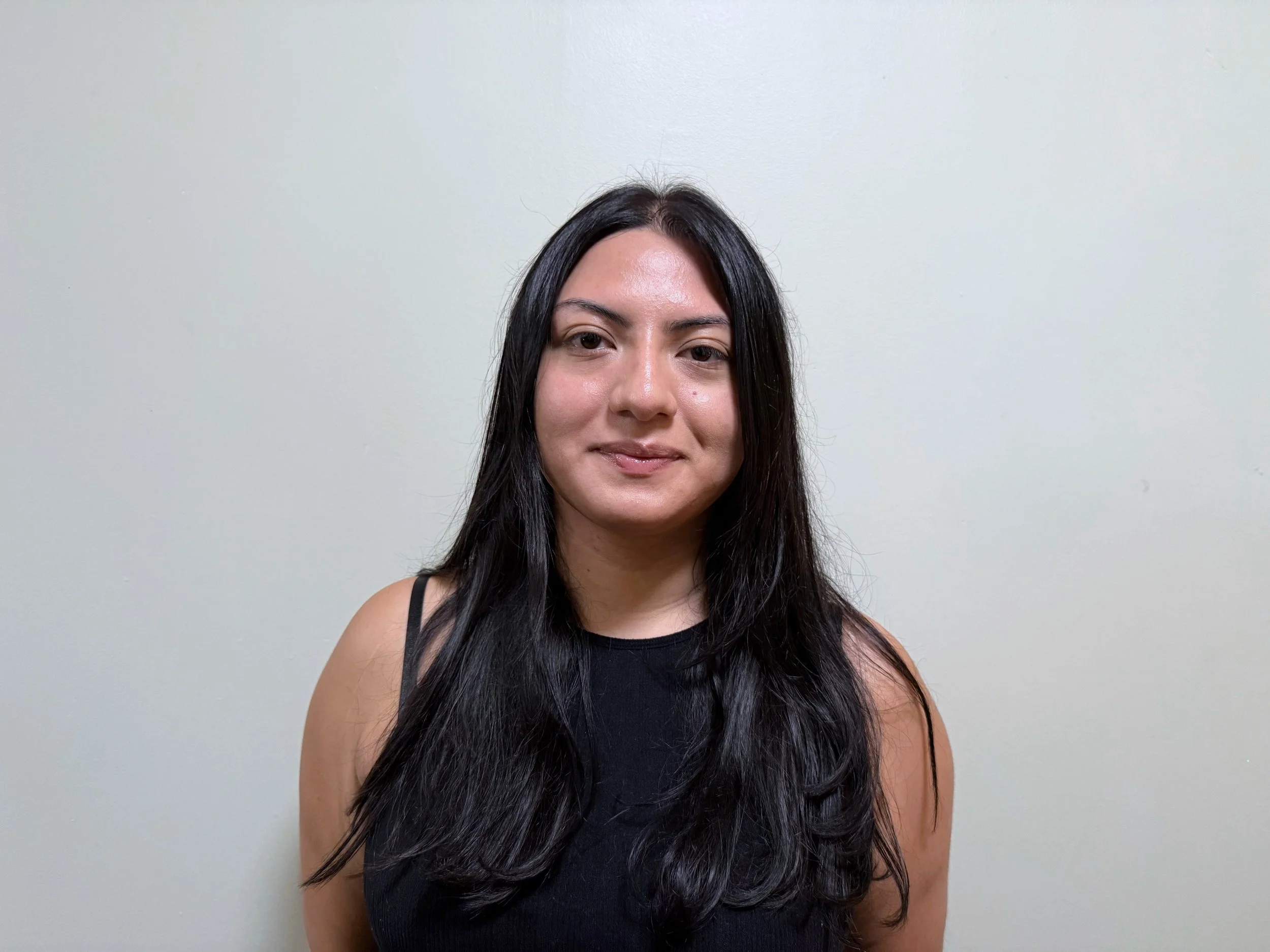 A young woman smiling with long black hair, in a black shirt, indoors