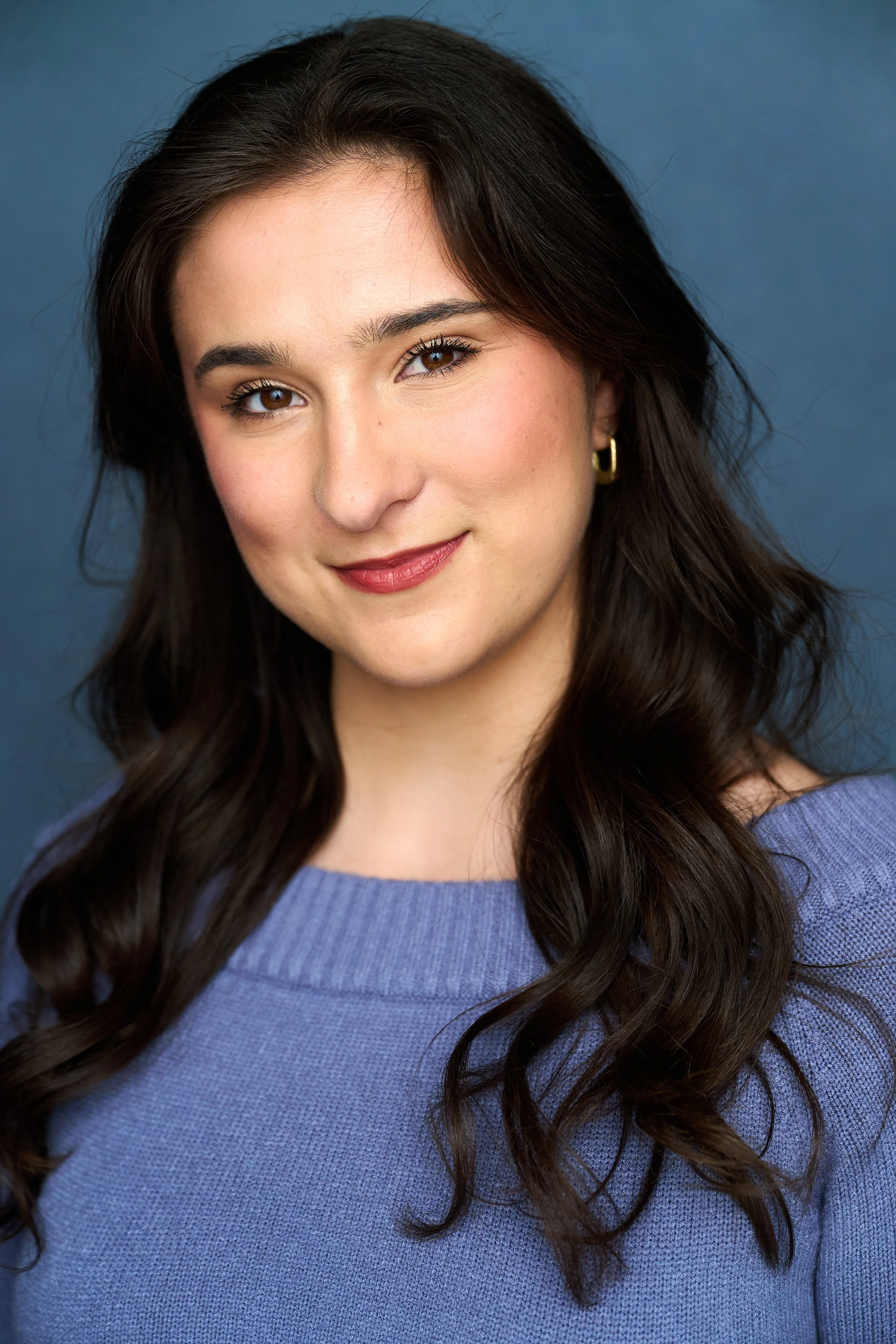 A young woman with long, curly dark hair, smiling, wearing a blue shirt