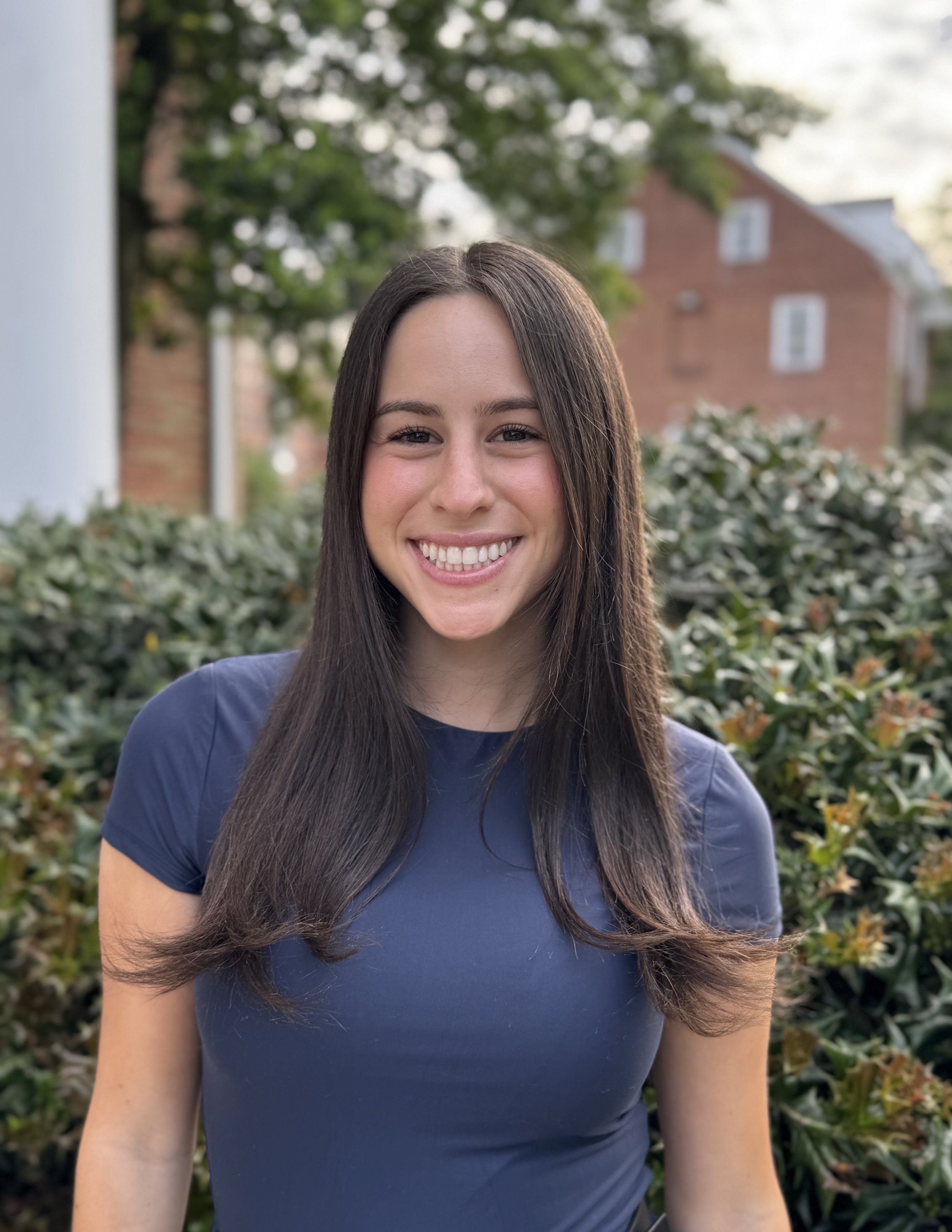 A young woman with brown hair, smiling, in a dark blue shirt