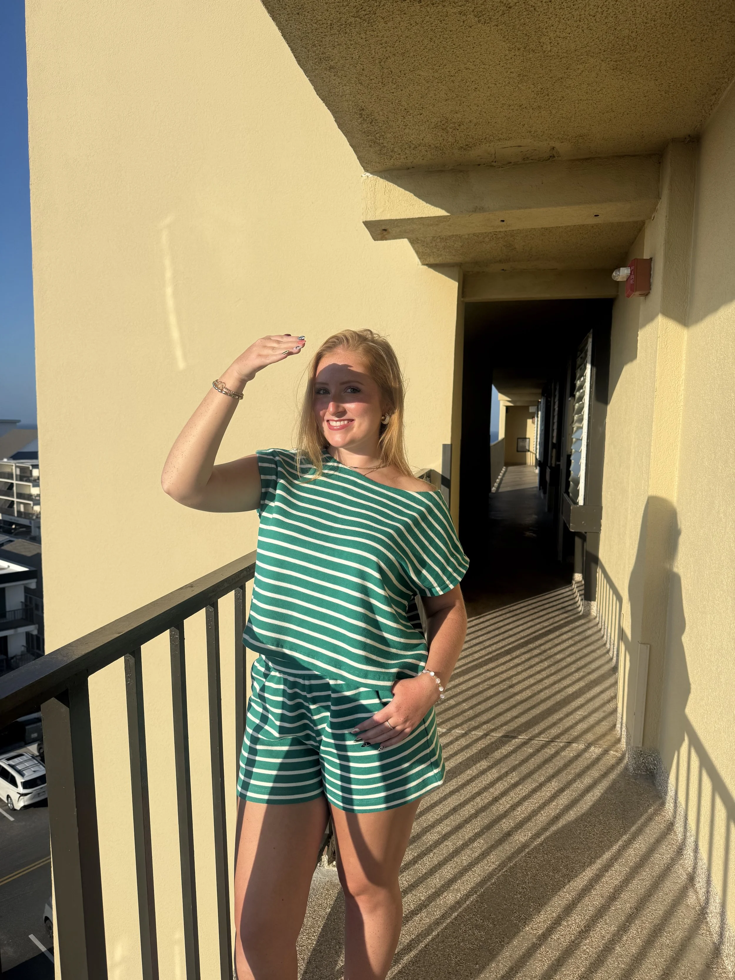 A young woman in a matching green t shirt and shorts set, with blond hair, smiling outside in the sunshine