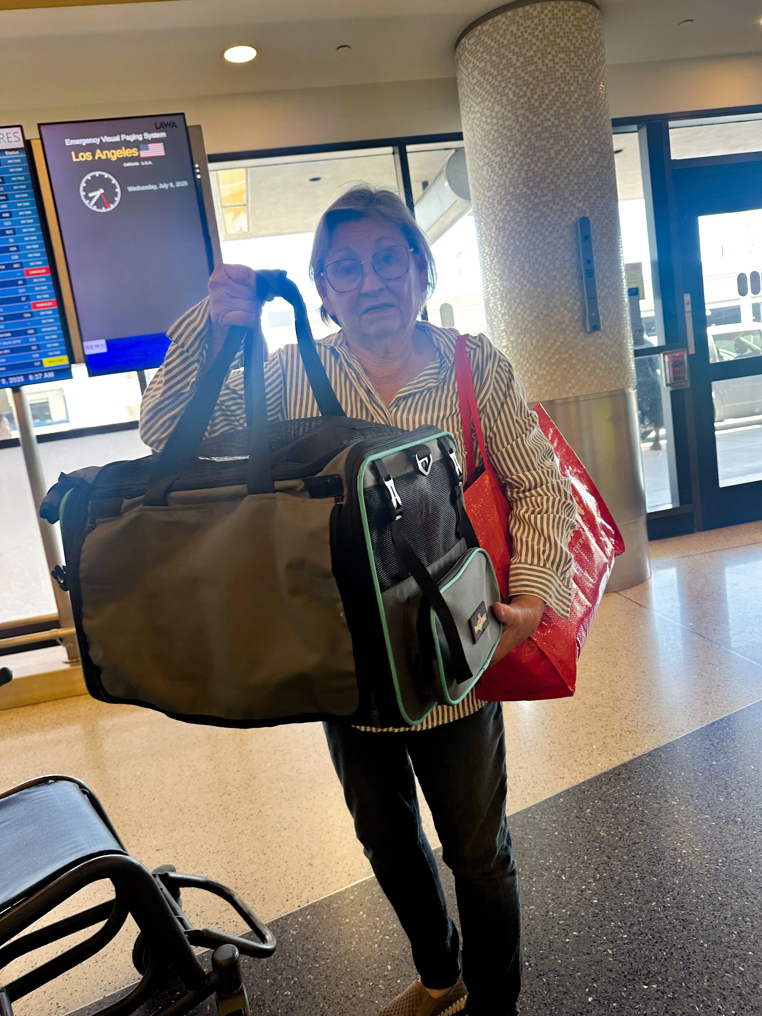 Flight nanny holding an airline-approved soft-sided pet carrier at an airport terminal while preparing for in-cabin pet transport.