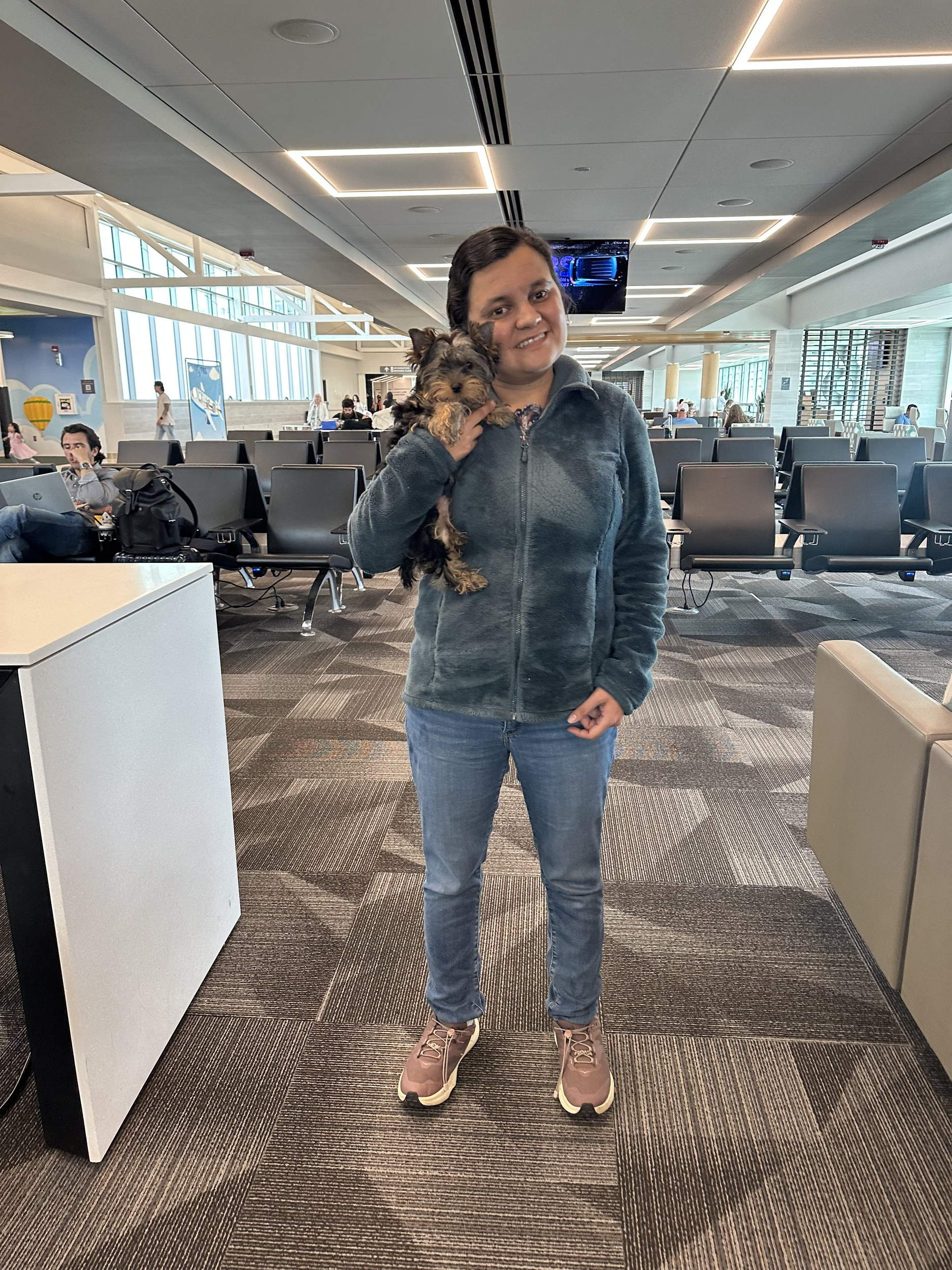 Flight nanny holding a small dog inside an airport terminal while offering in-cabin pet transport services from Southern California.
