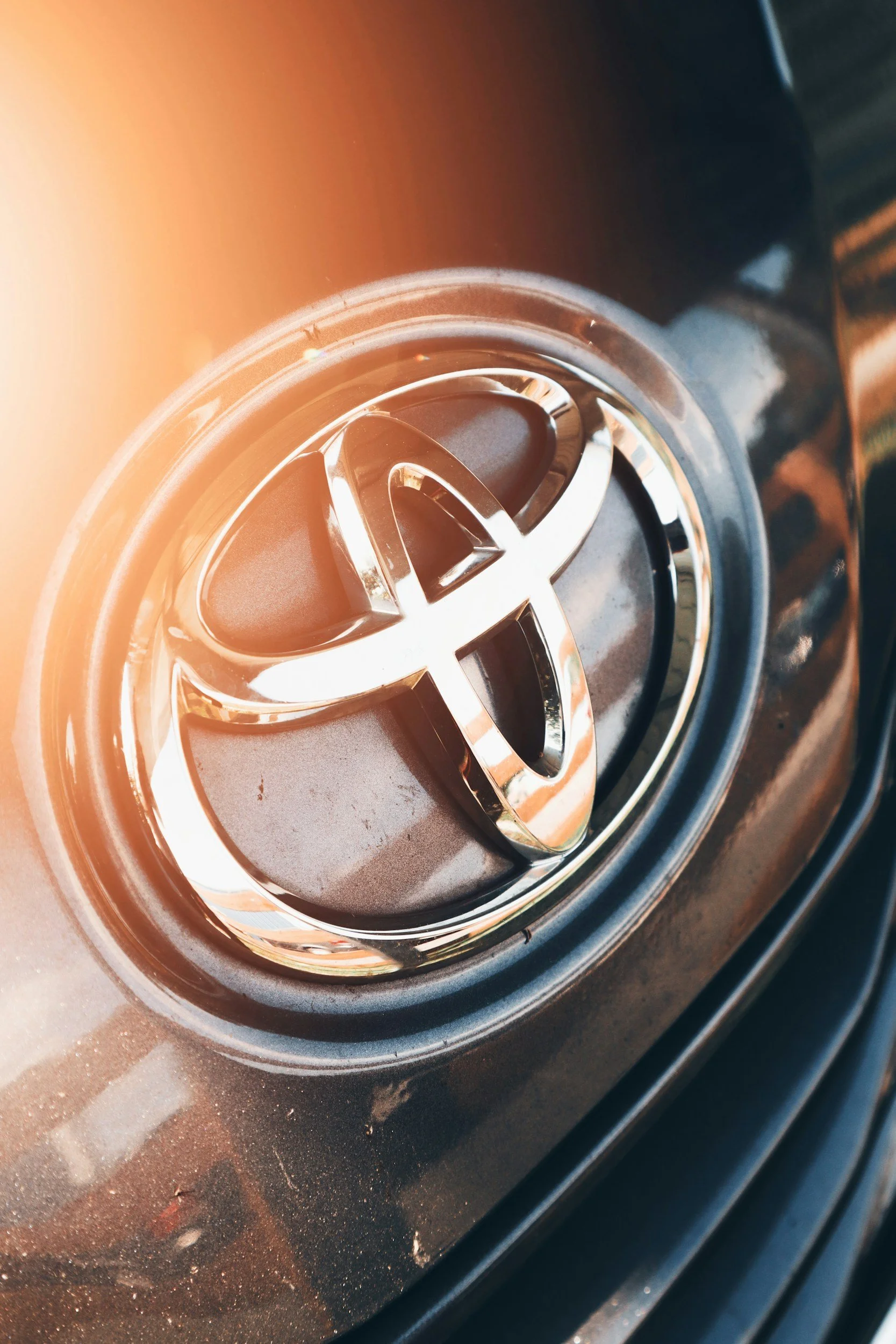 Close-up of the Toyota logo on a car's front grille with sunlight glare.