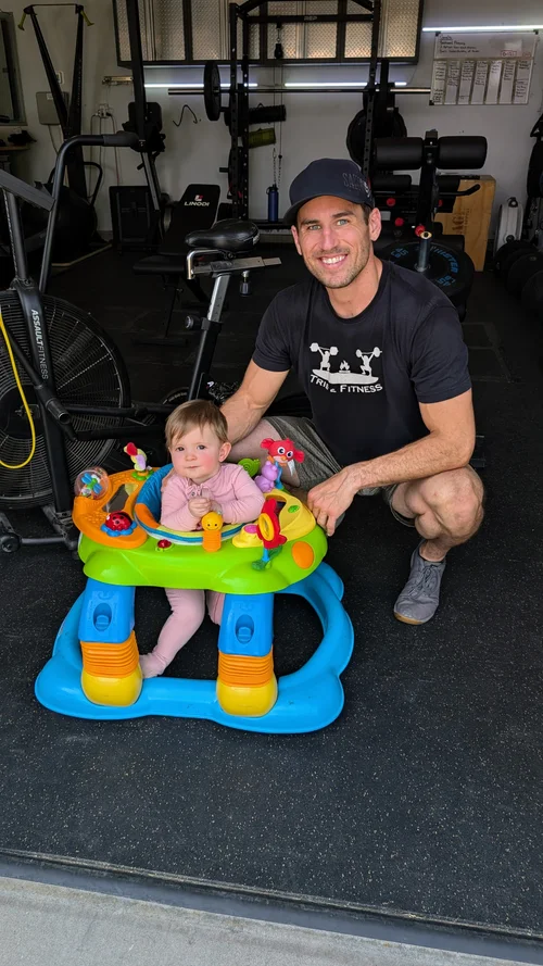 Sam Moses kneeling next to his baby daughter in the gym