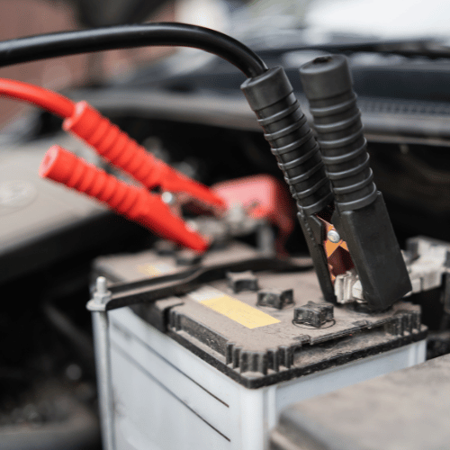 Car battery connected to jumper cables in a vehicle engine bay.