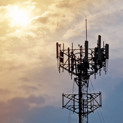 Cell tower silhouette against a sky with clouds and the sun.
