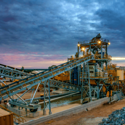 Industrial processing plant with conveyor belts and machinery under a cloudy sky at sunset.