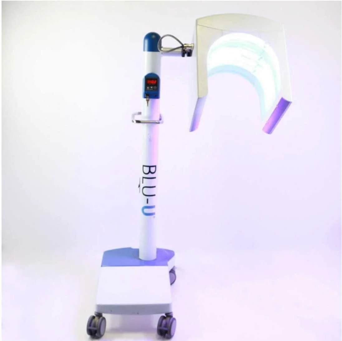 Medical device on a white background, with a tall stand labeled 'BLU-U,' a mounted light, and a transparent mask with a rainbow-colored glow.