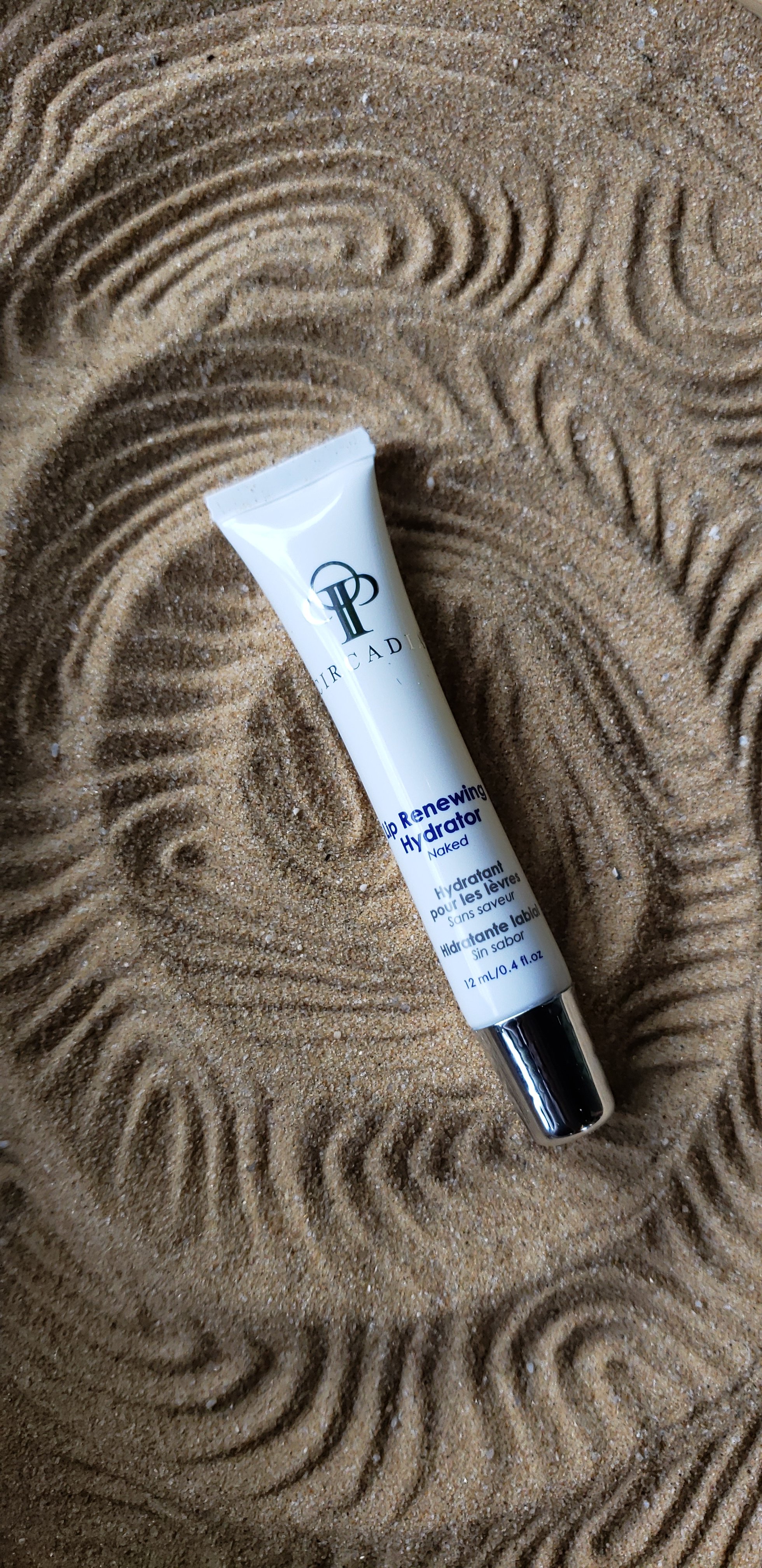 Lip serum laying in a bed of neutral colored sand with a lined design in the sand 