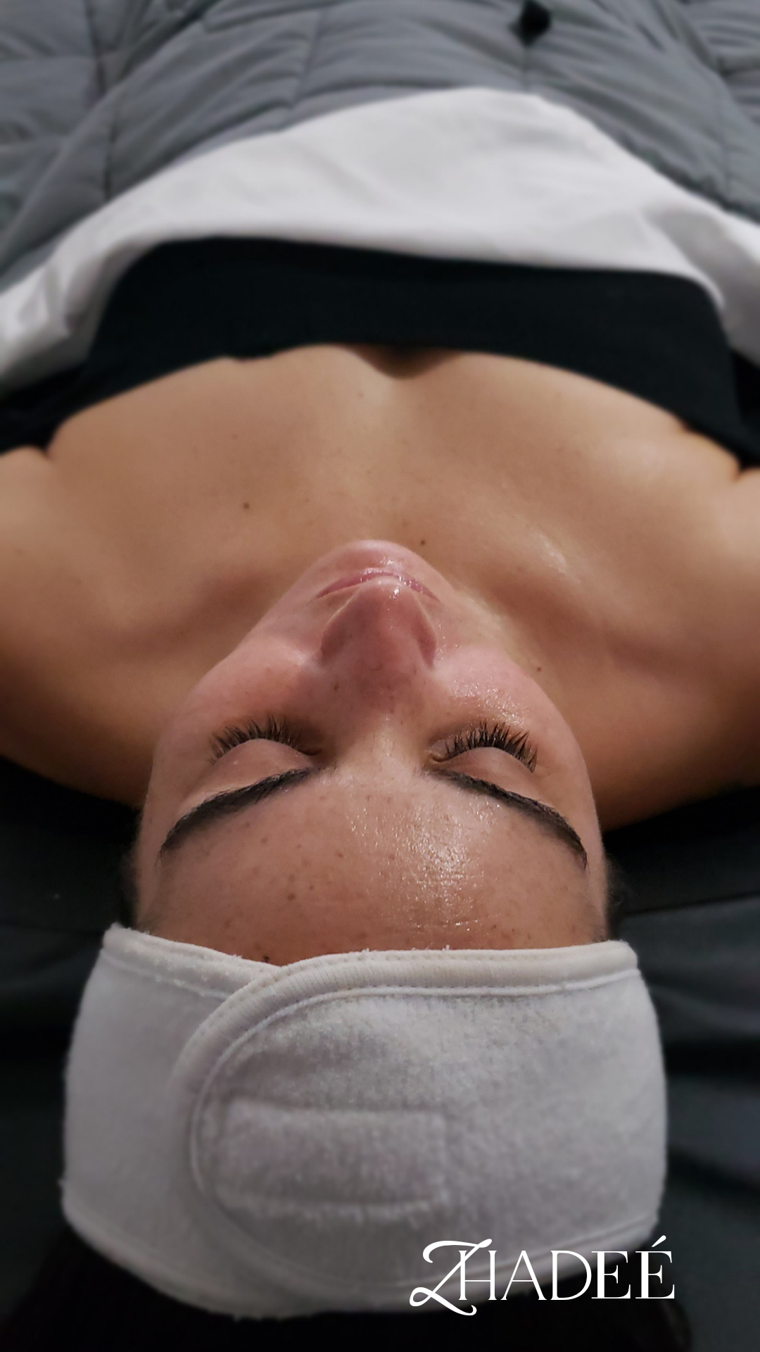 Person lying on a spa bed wearing a white headband with eyes closed, receiving a facial treatment.