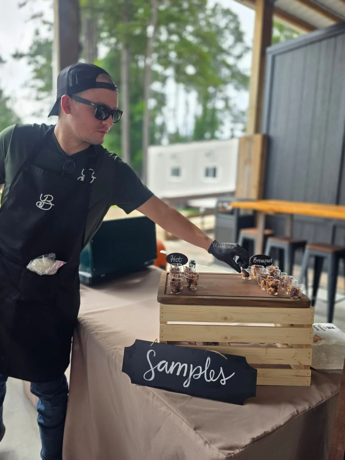 Bruno arranges product samples and display items on a wooden crate at the Y&B Farms market booth, preparing for customer visits.