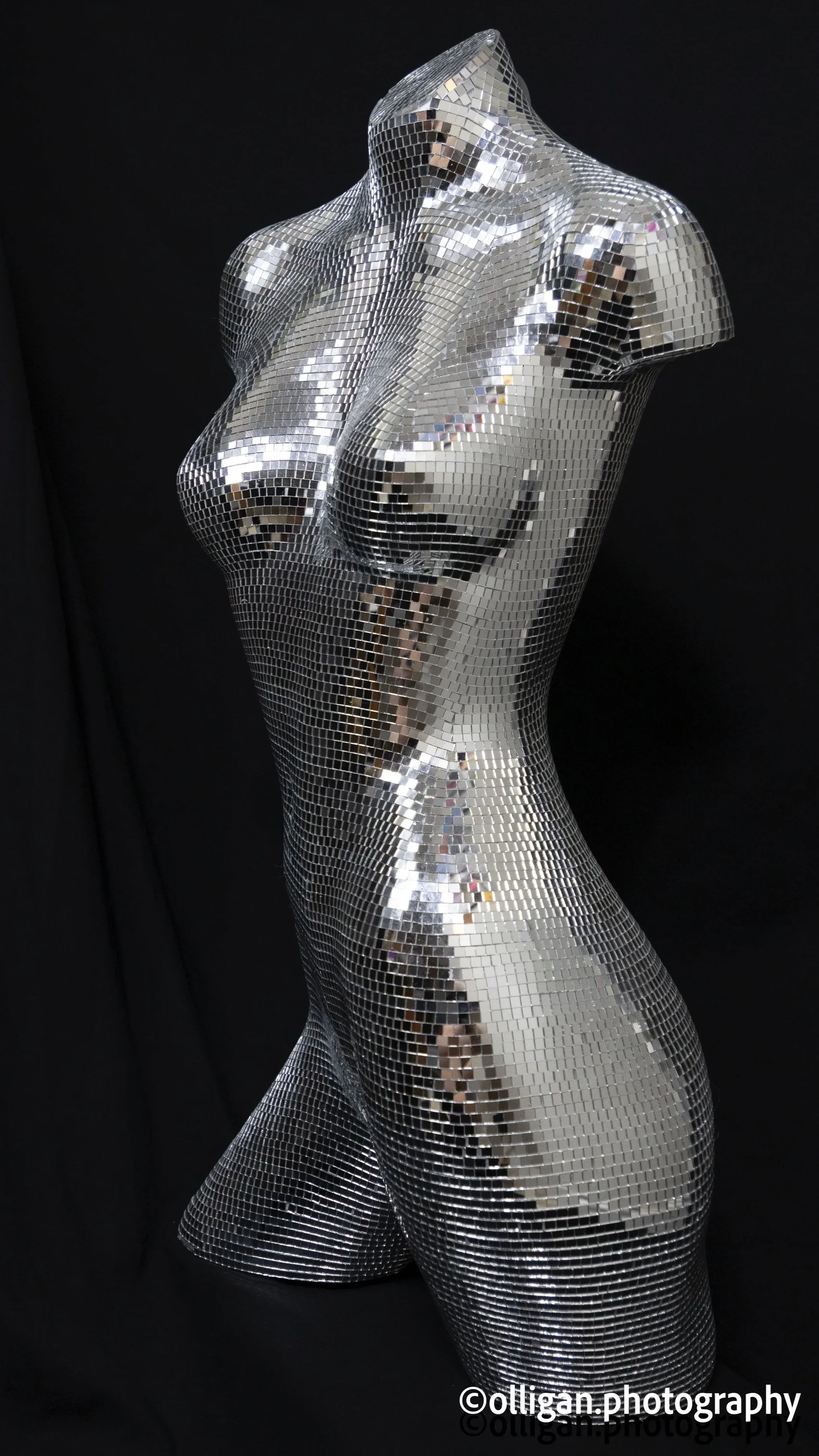 A disco mirrored glass tiled , mosaic-style sculpture of a female torso mannequin on a black background ready for the party or club scene.