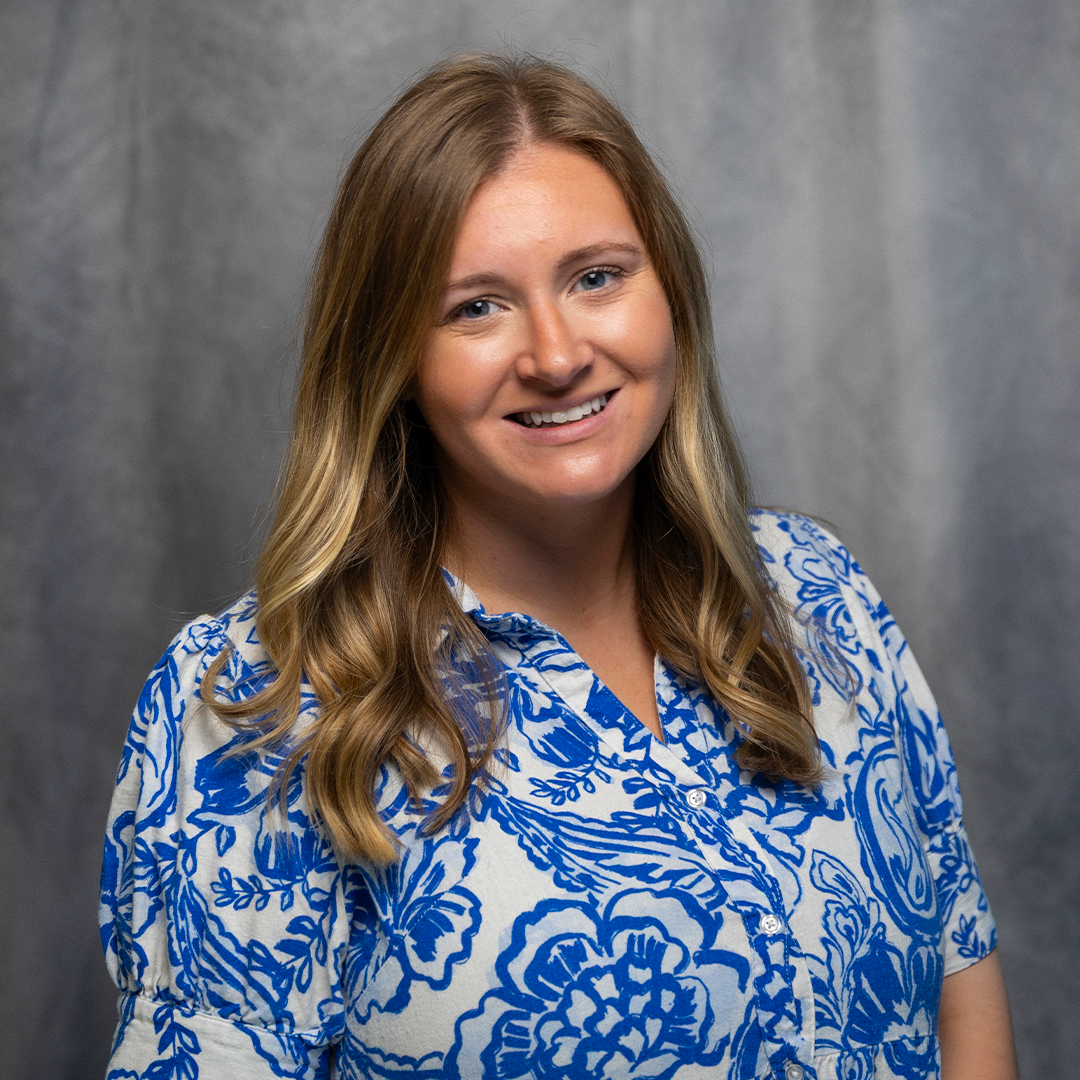 A woman with blonde hair smiling at the camera, wearing a grey turtleneck sweater.