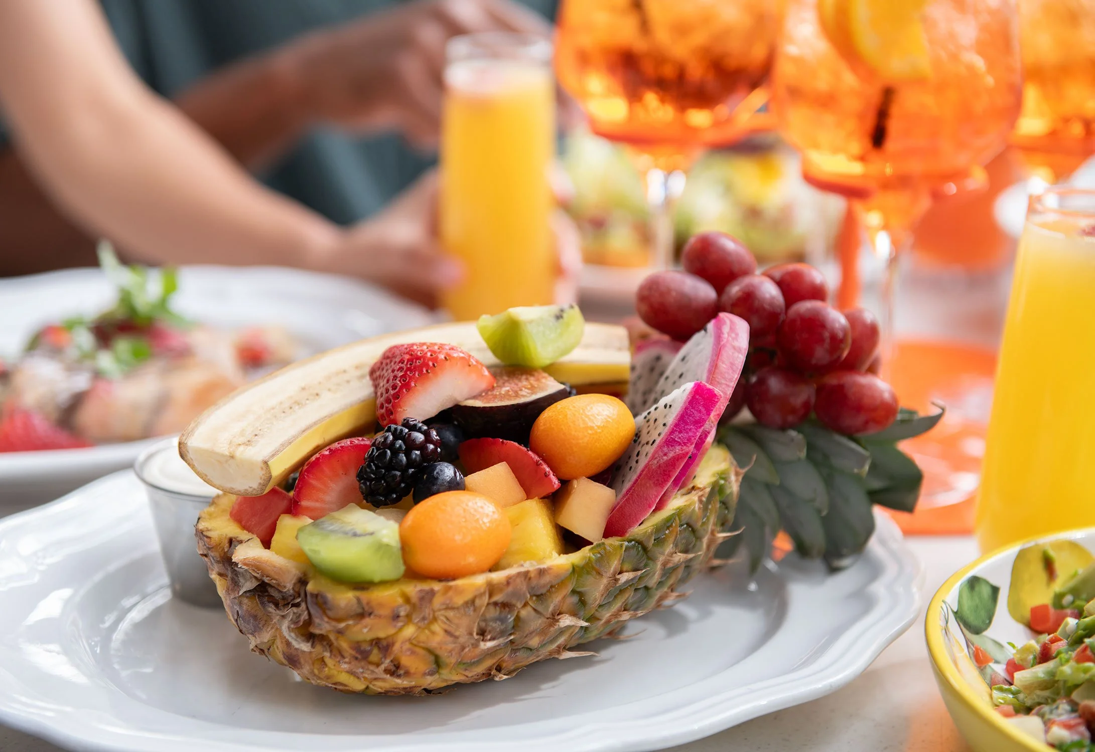 A hollowed-out pineapple filled with an assortment of fresh fruits including strawberries, grapes, kiwi, dragon fruit, and melon, serving as a tropical fruit display on a white plate at Cheri Rooftop during brunch.