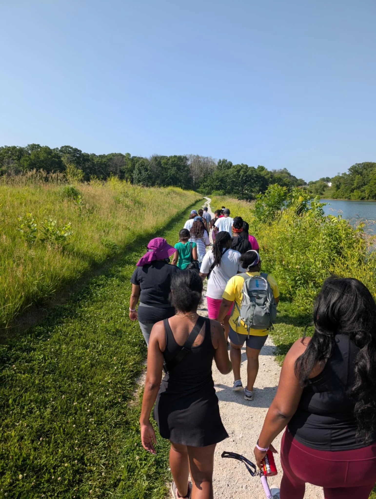 A group of people walking on a trail along a river on a sunny day.