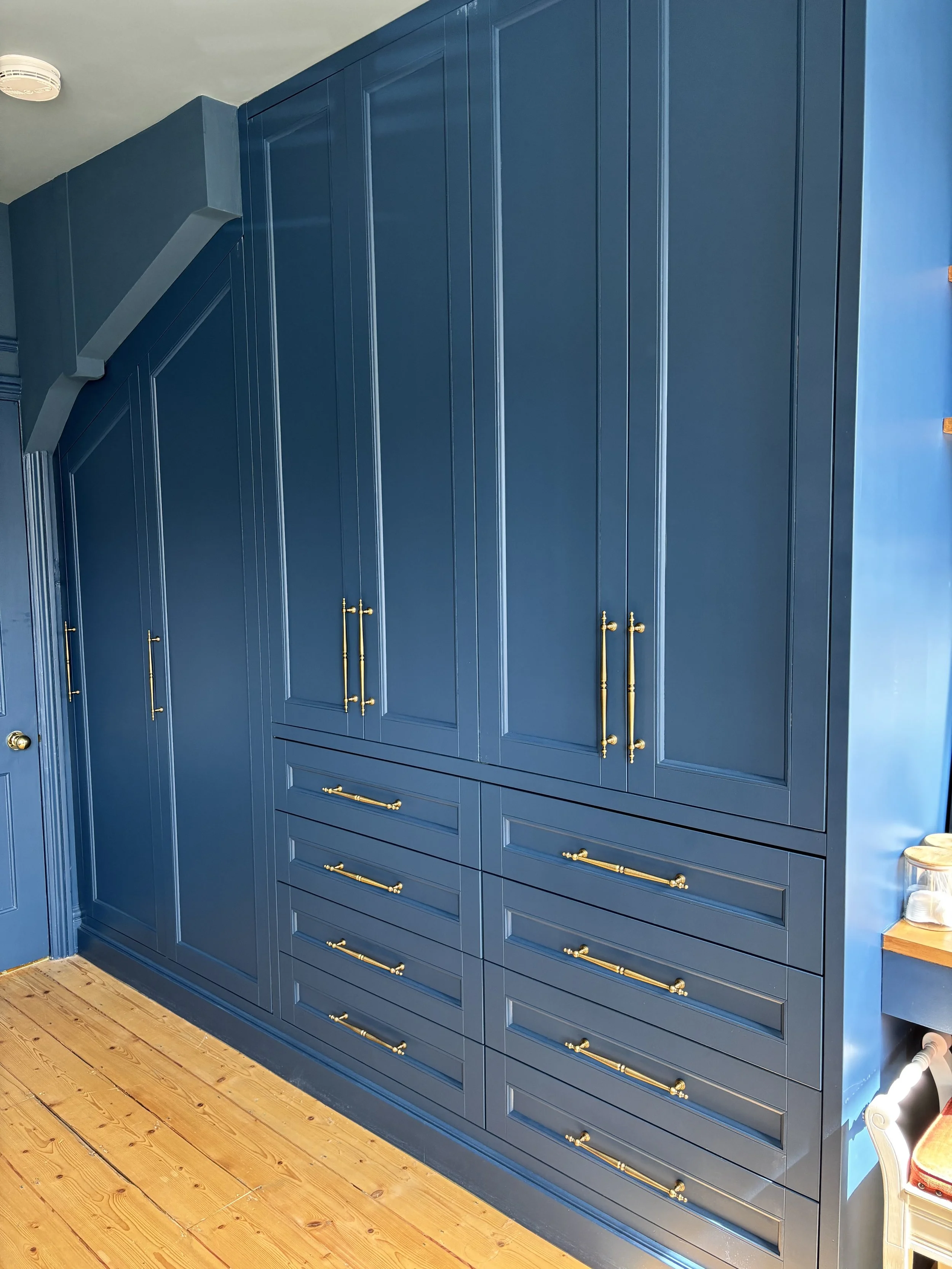Blue built-in cabinetry with gold handles in a room with wooden flooring.