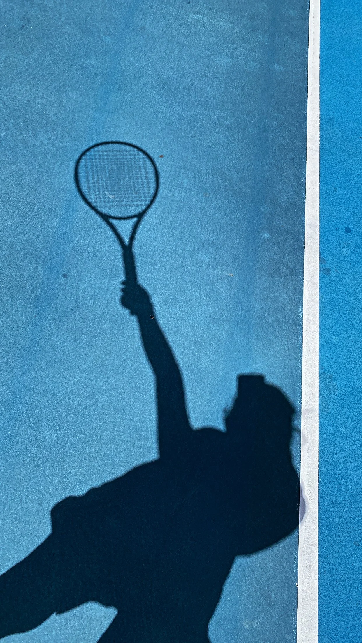 Silhouette of a person holding a tennis racket during a match on a blue tennis court, casting a shadow.