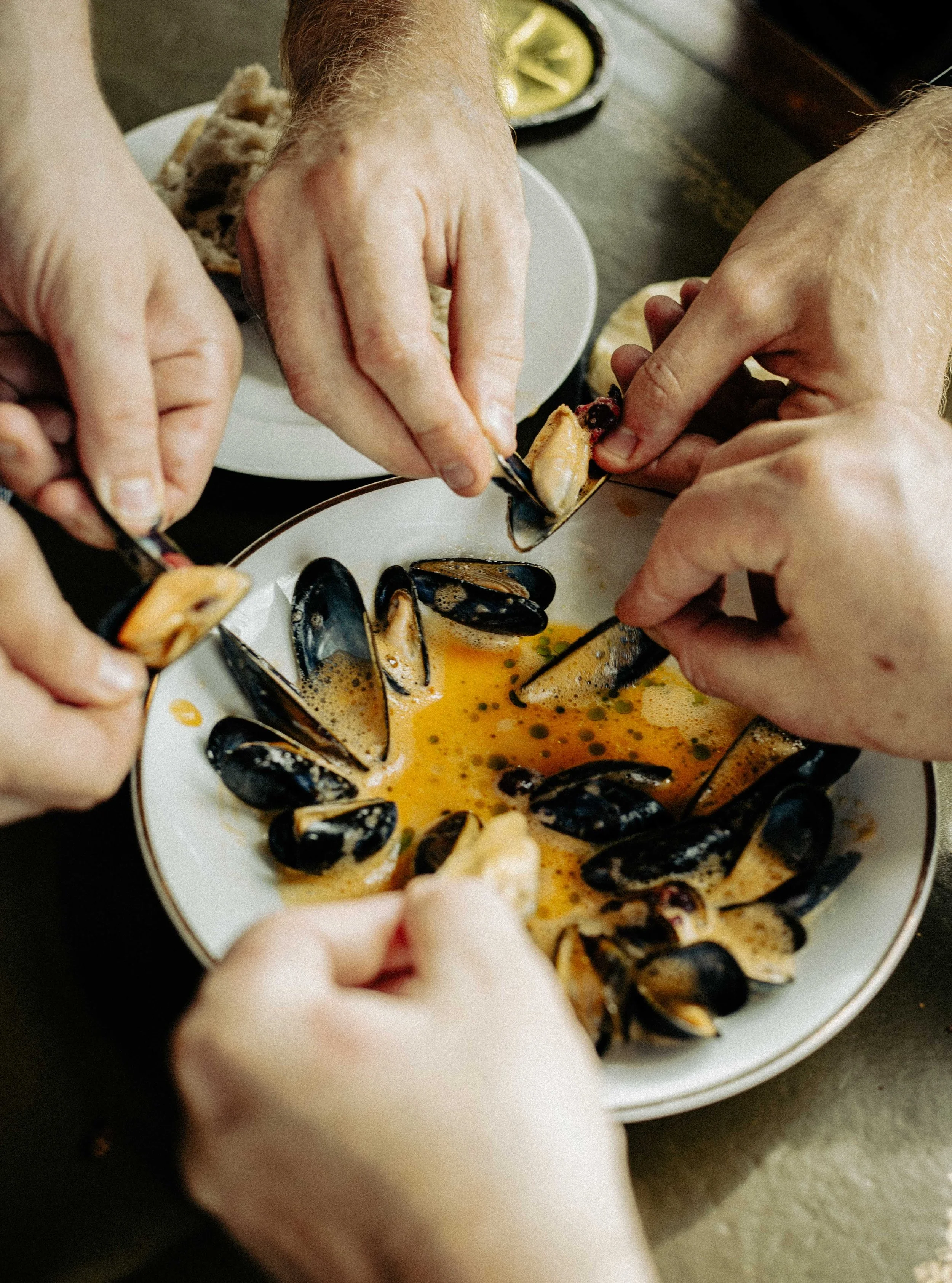 Verschillende mensen die mosselen uit een schaal halen en bereiden in een schaal met een saus of bouillon.