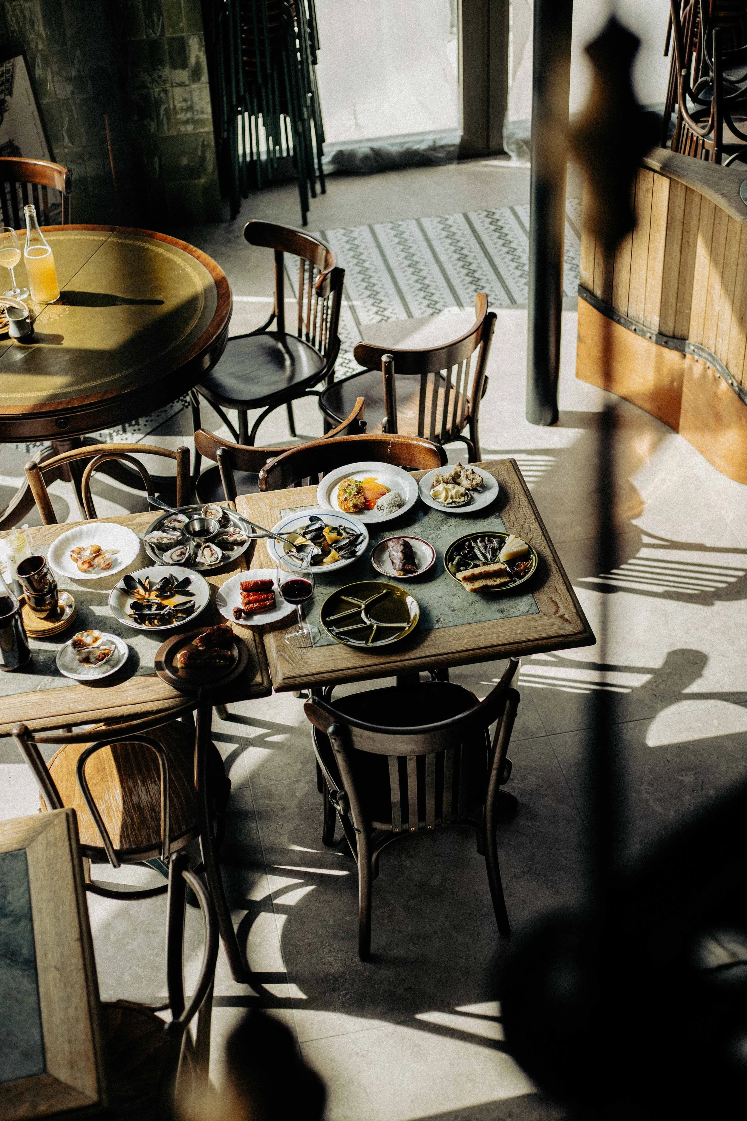 Tafel met diverse zeevruchten en wijn in een restaurant, zonnelicht en schaduwen op de vloer.