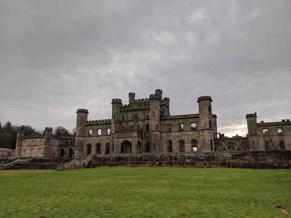 Exterior of a stone castle with towers and arches against a cloudy sky.