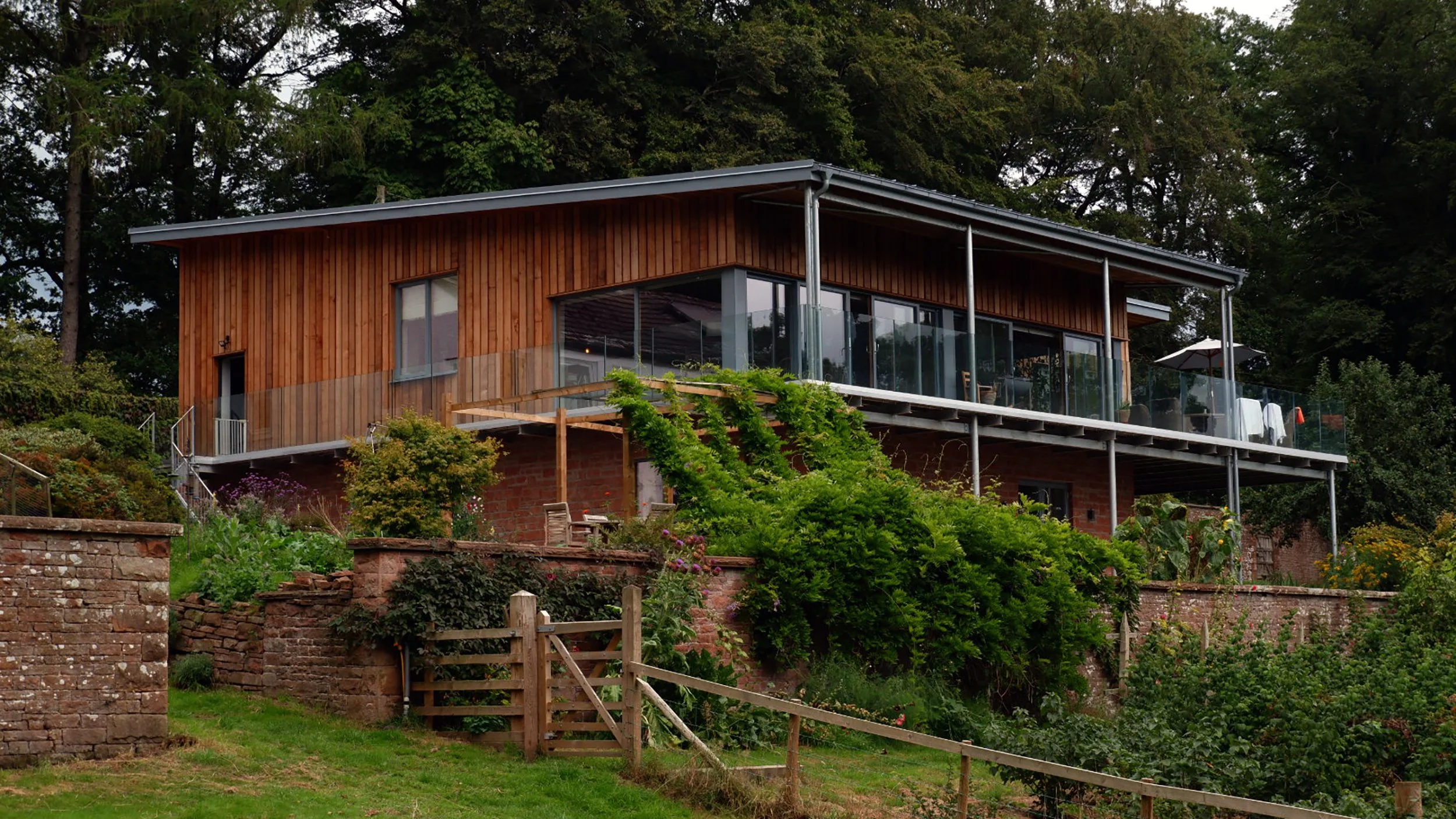 Timber frame new build house in Cumbria with contemporary architecture, modern, timber clad, lazonby sandstone walls, glass balcony, raised seam steel roof. Timber frame by Builders near Welshpool, Shrewsbury, Oswestry. Ty Cefn Ltd