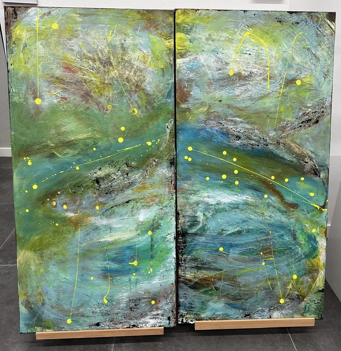 Abstract painting with green, blue, and yellow hues, featuring splashes and strokes with yellow dots and lines on two panels.