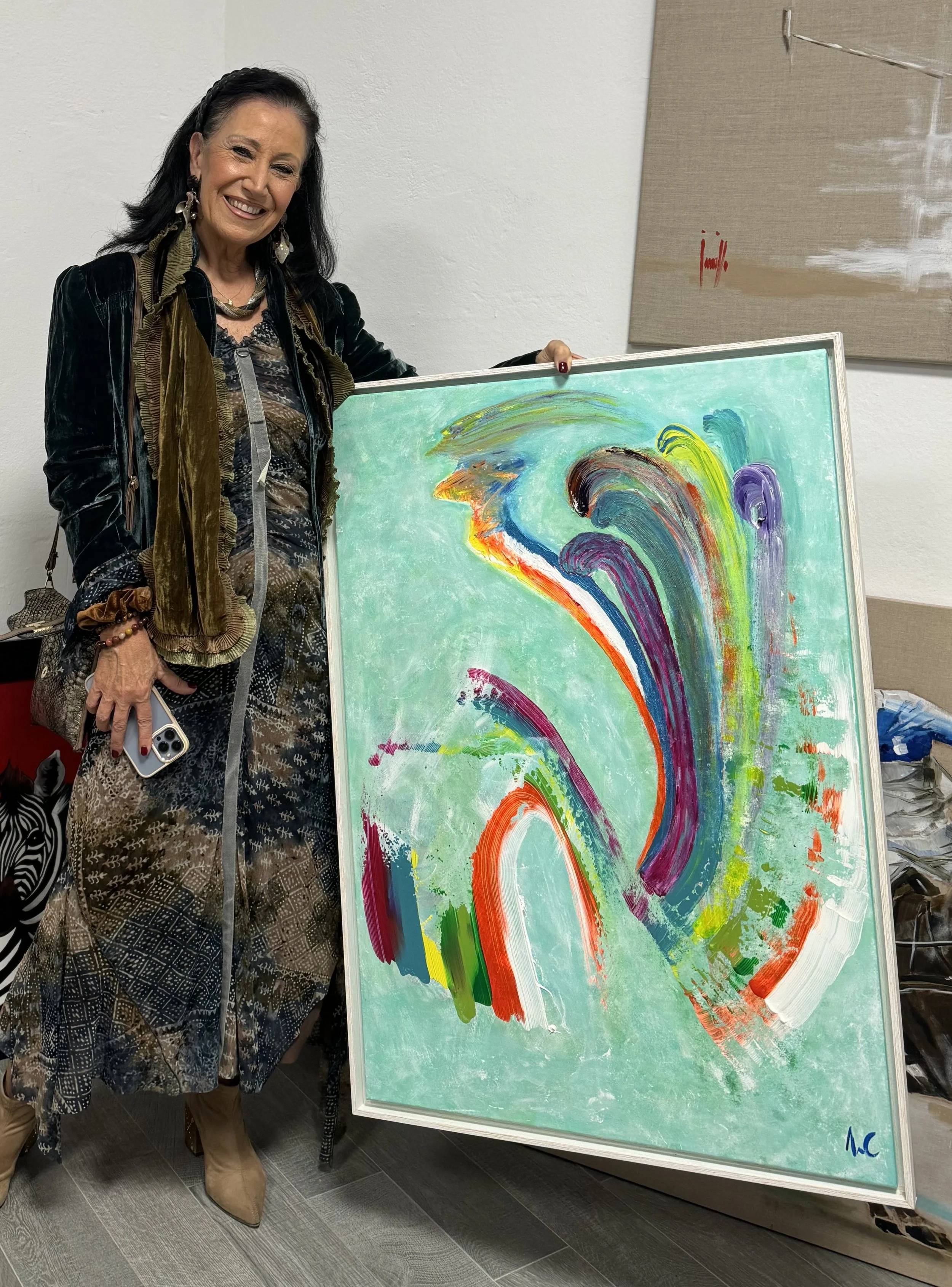 Woman holding an abstract painting with colorful brush strokes on a teal background.