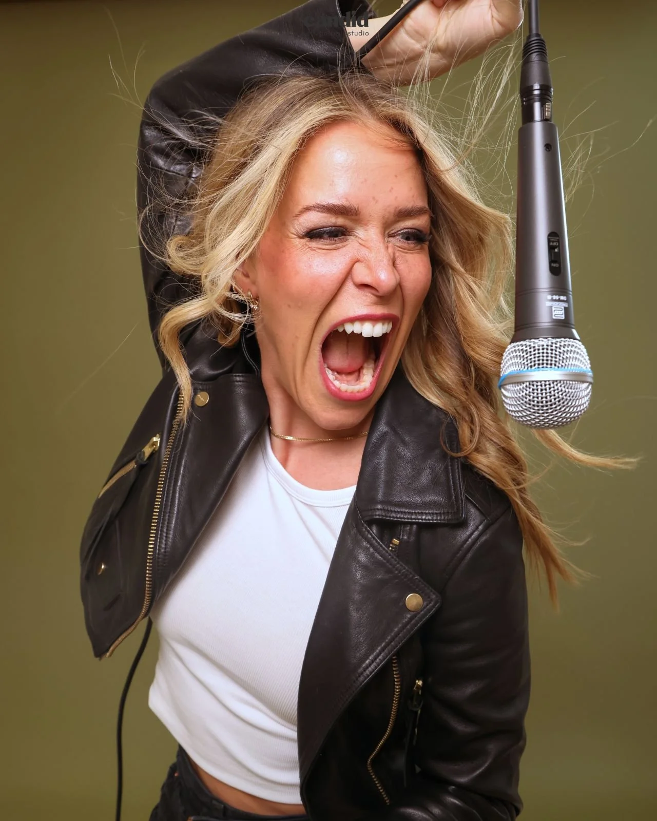 a woman in candid self-portrait studio posting with a microphone and a wind fan in her hair looking happy
